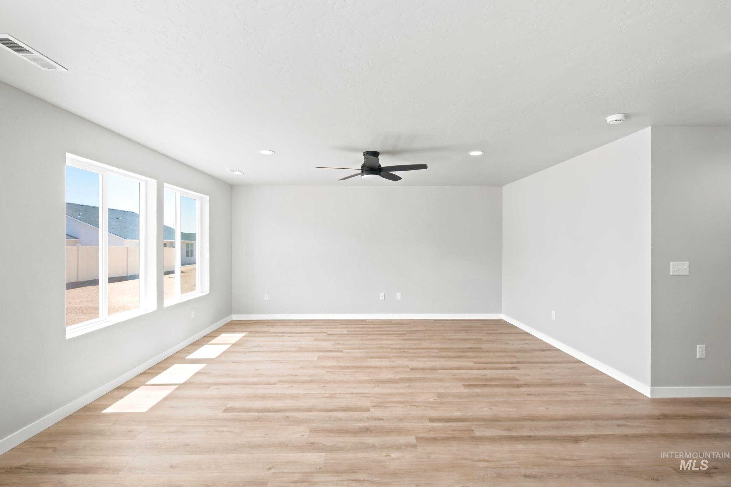 Spacious room featuring wood-finish flooring, multiple windows, a ceiling fan, recessed lighting, and white baseboards