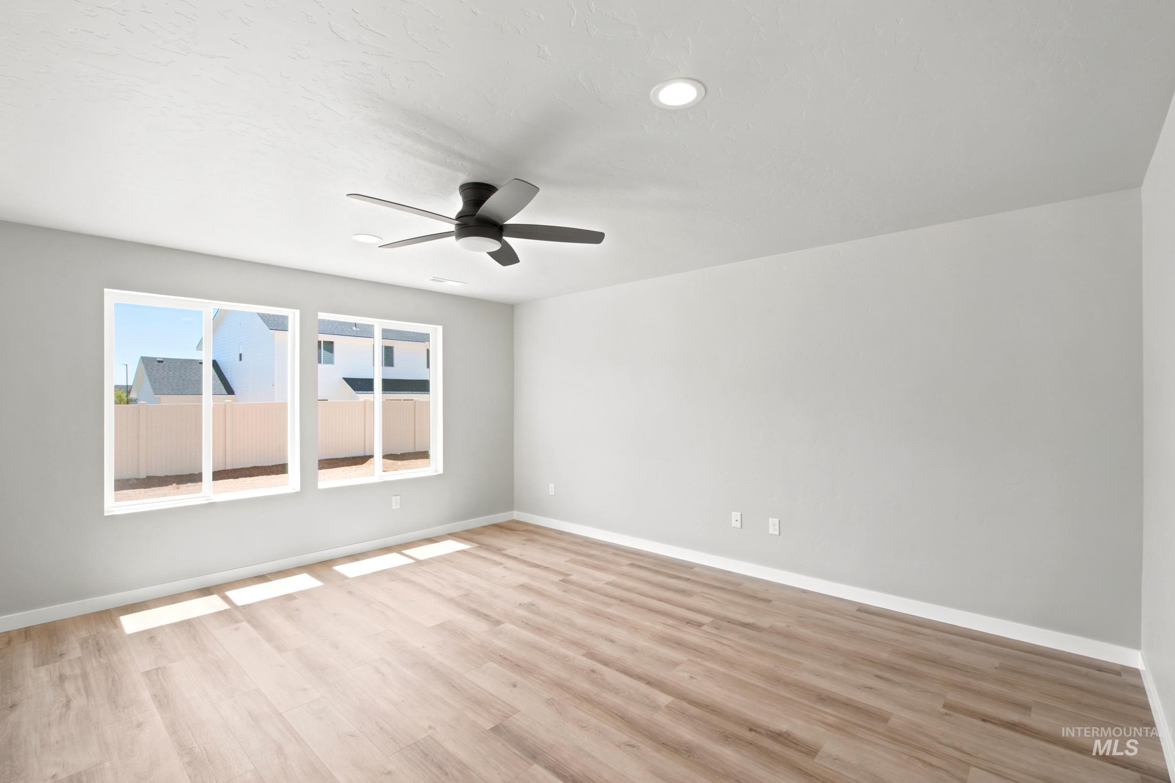 Spacious room featuring light wood-finish flooring, two large windows, a ceiling fan, and recessed lighting