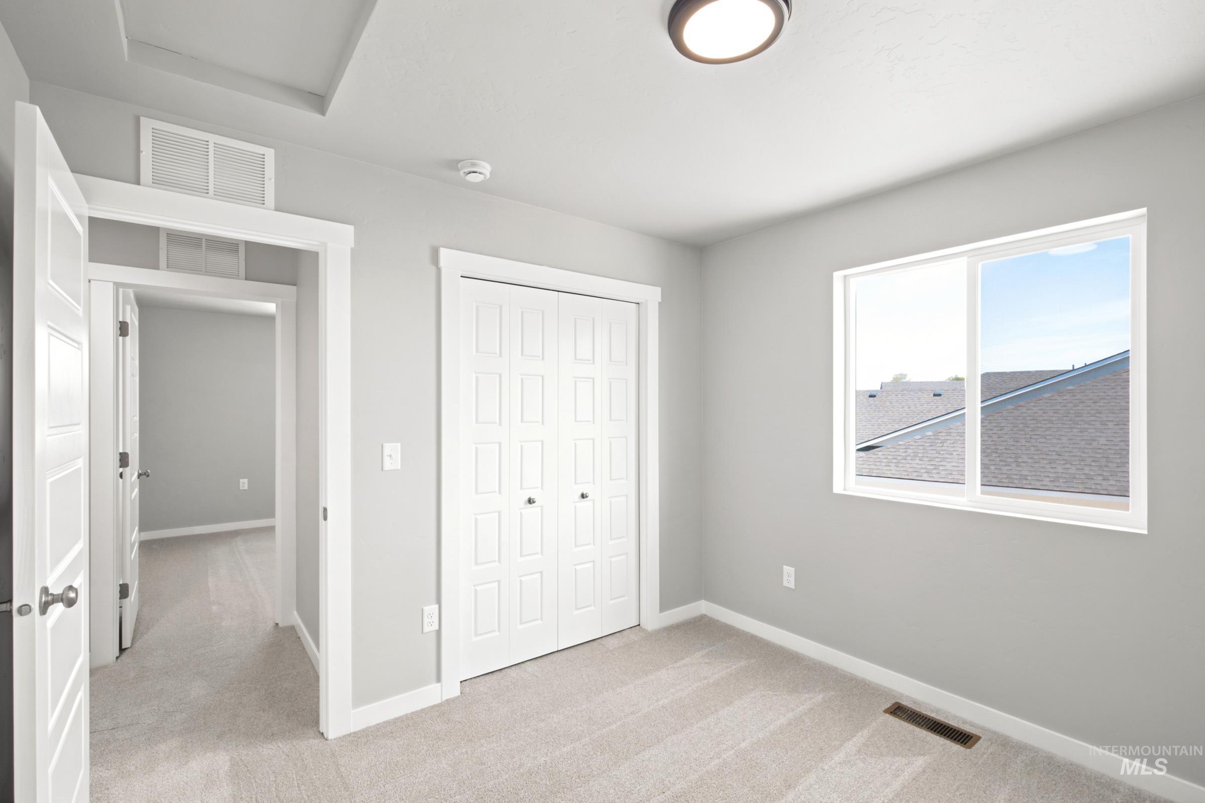 Room featuring light gray walls, light-colored carpet, a double-panel bifold door closet, a window with white trim, and a flush-mount ceiling light fixture