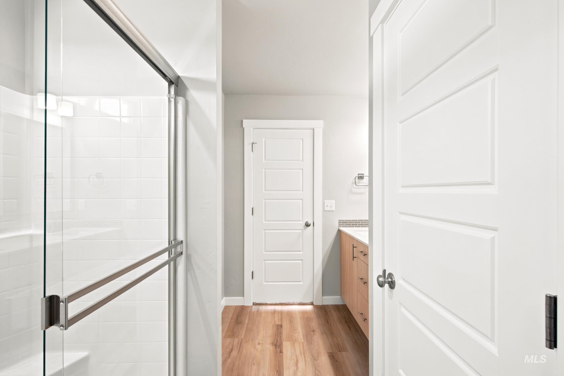 Glass-enclosed shower with white subway tile surround, wood-finish flooring, and white paneled doors
