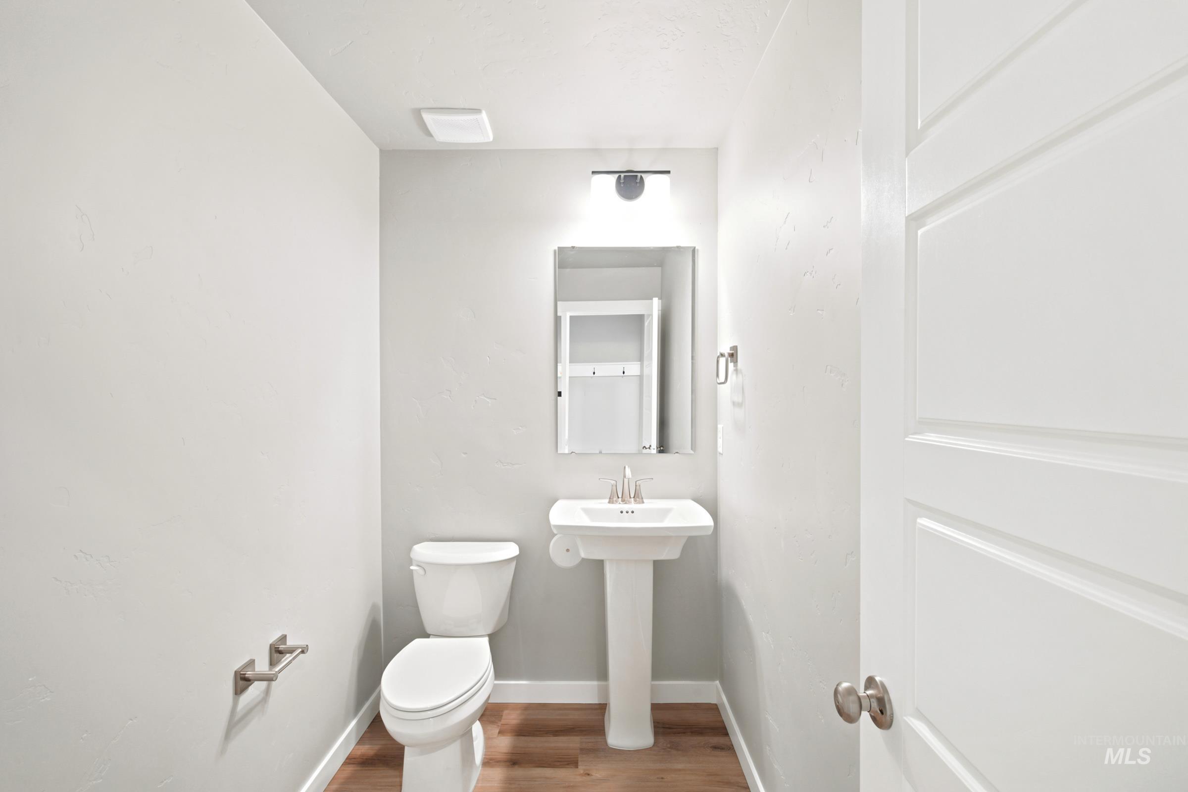 Powder room featuring a white pedestal sink, white toilet, and wood-finish flooring