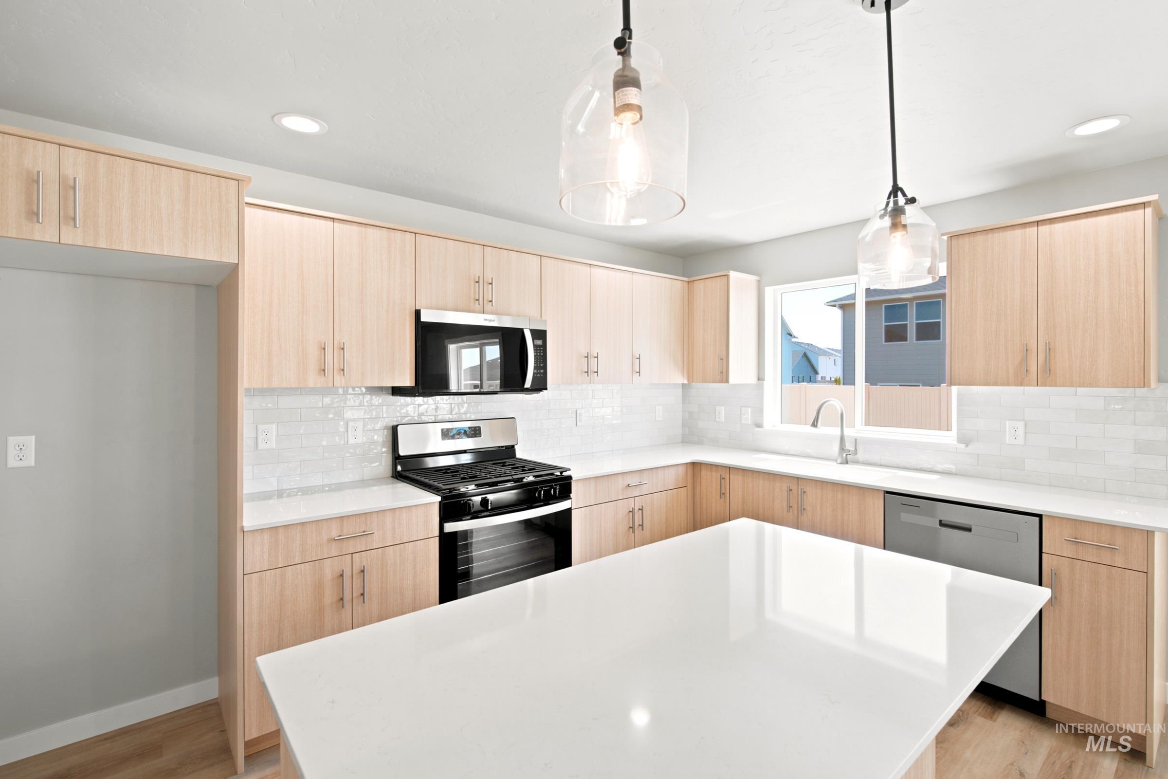 Modern kitchen featuring light wood-finish cabinetry, white countertops, subway tile backsplash, stainless steel appliances, and a central island