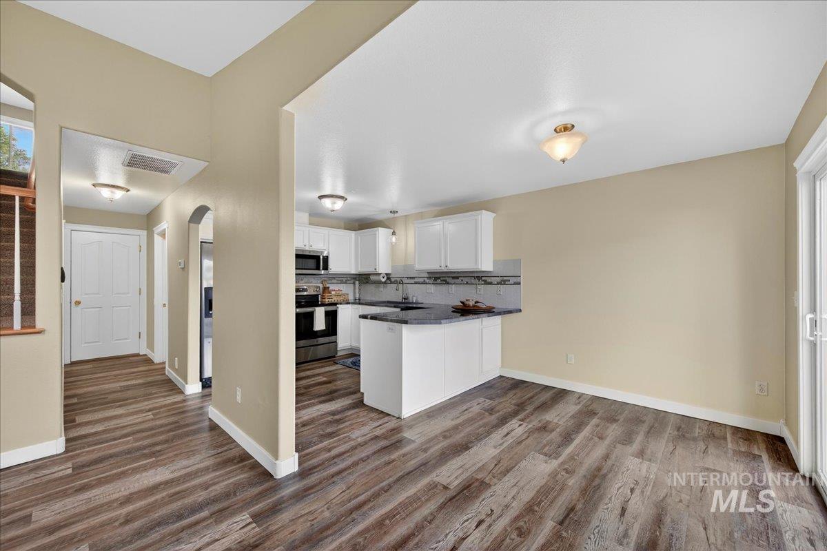 Kitchen featuring a peninsula, white cabinetry, stainless steel appliances, decorative backsplash, and arched walkways