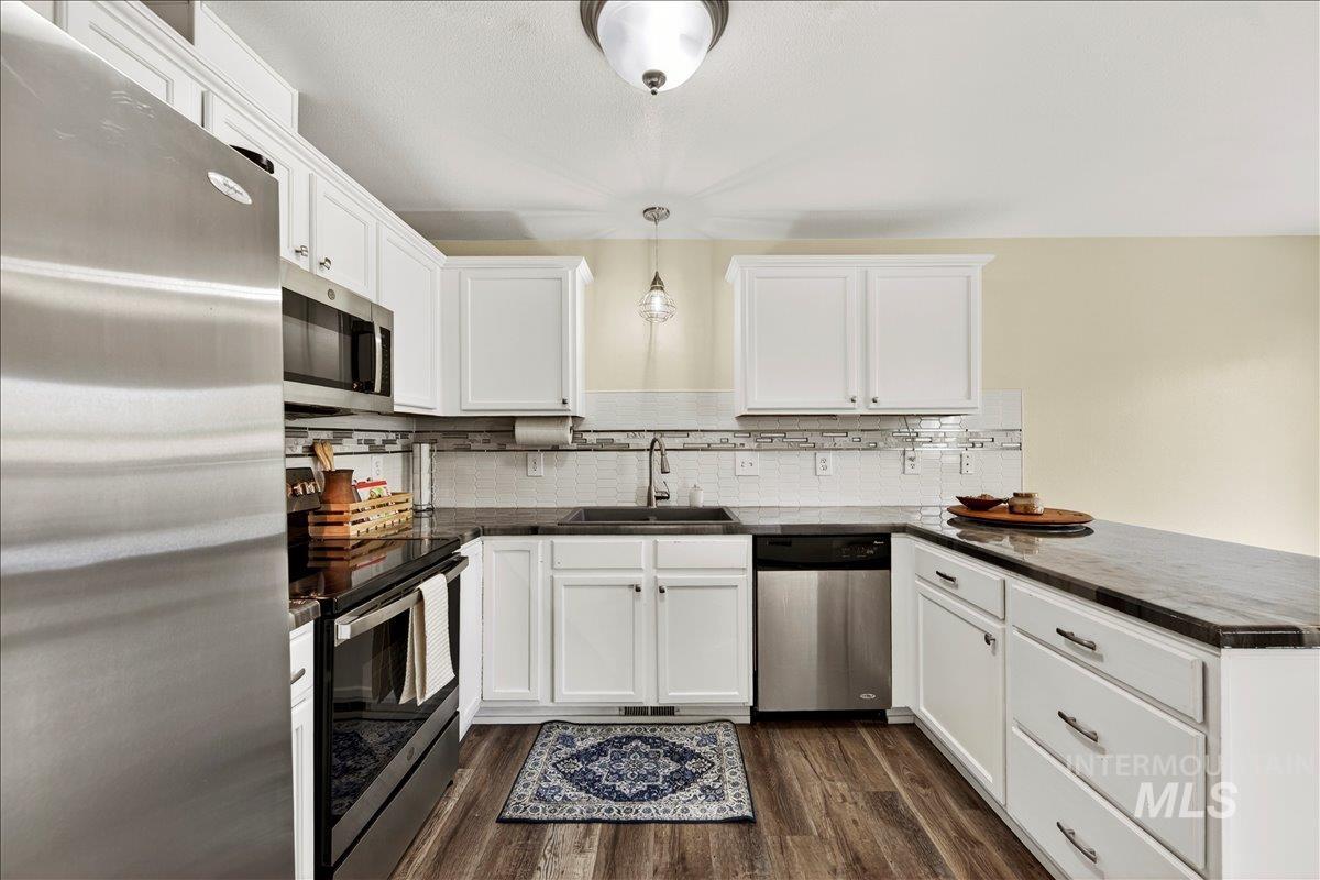 Kitchen with stainless steel appliances, dark countertops, white cabinetry, and dark wood-style floors