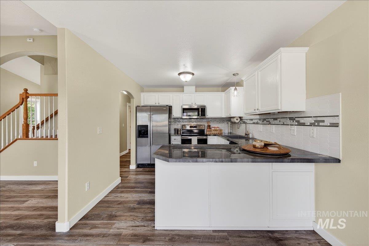 Kitchen featuring arched walkways, stainless steel appliances, white cabinetry, and tasteful backsplash