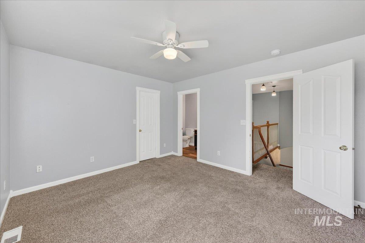Unfurnished bedroom with carpet, ensuite bathroom, and a ceiling fan