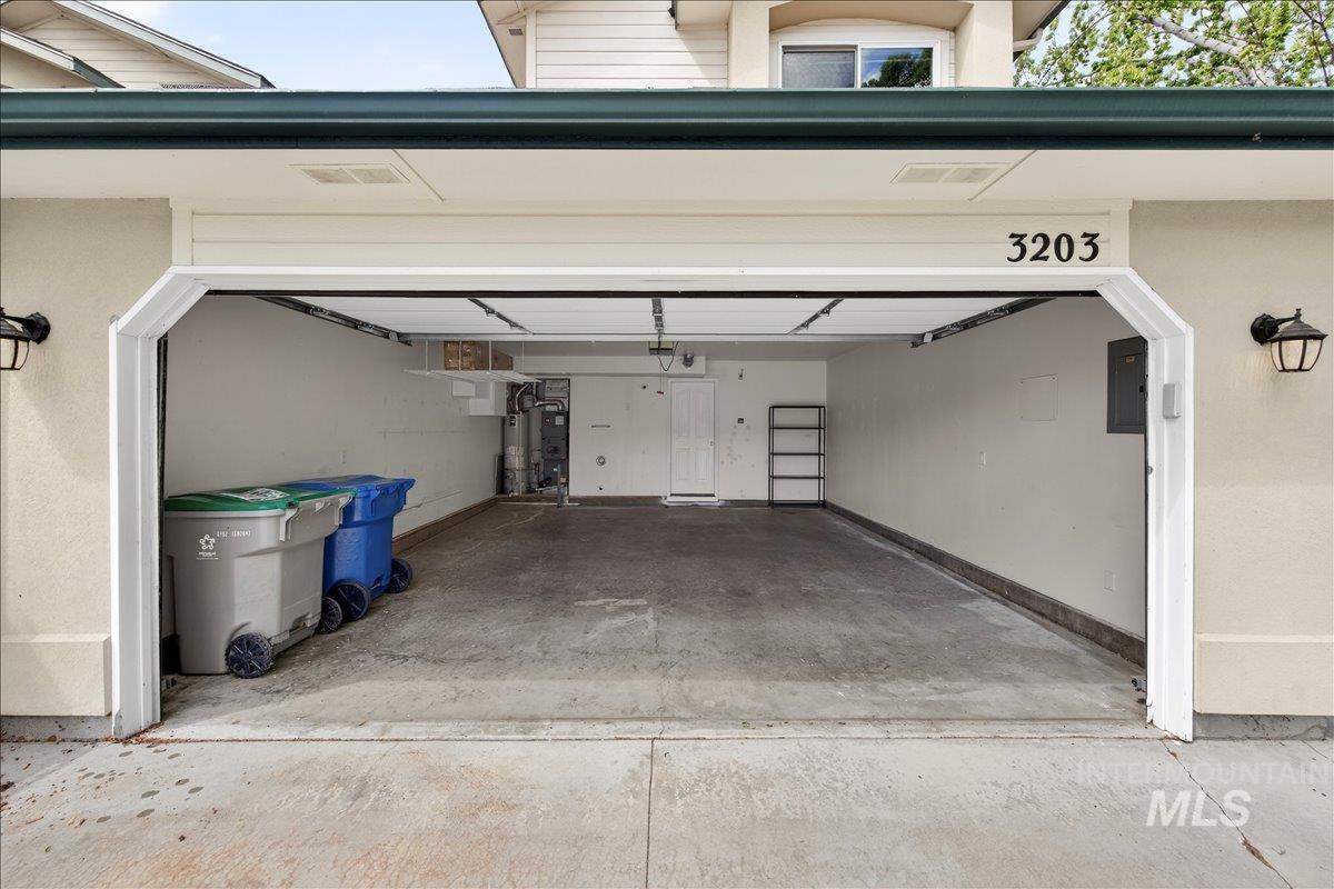 Garage with electric panel, driveway, and gas water heater