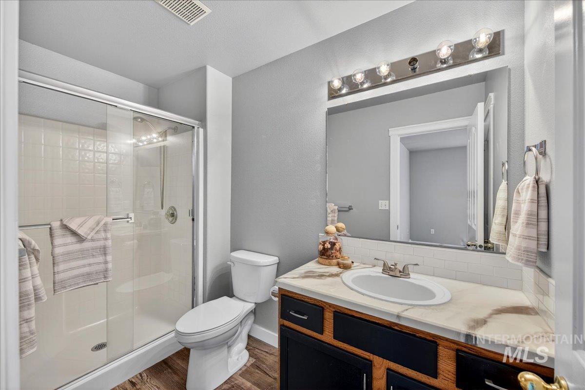 Bathroom with a textured wall, vanity, a stall shower, and dark wood-style floors
