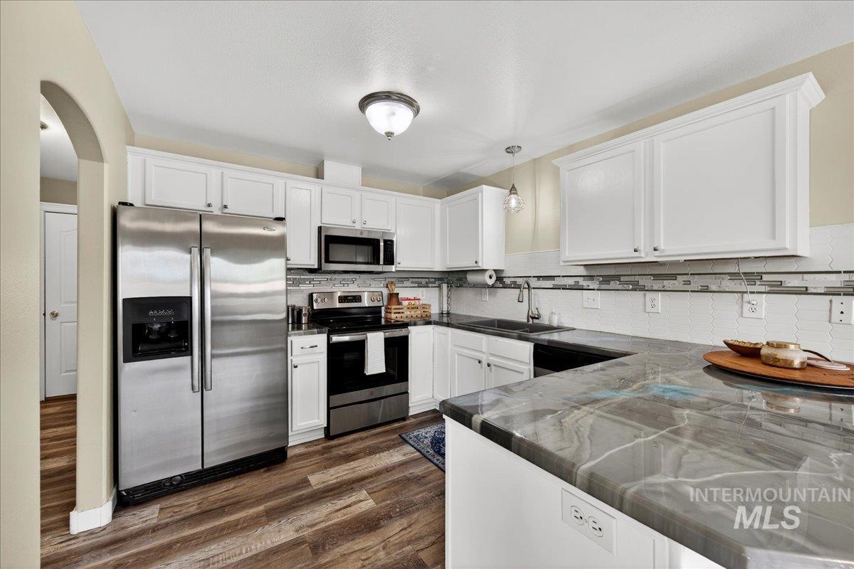 Kitchen featuring stainless steel appliances, white cabinetry, arched walkways, and pendant lighting