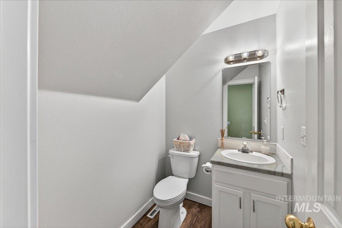 Half bath featuring a textured wall, vanity, and dark wood finished floors