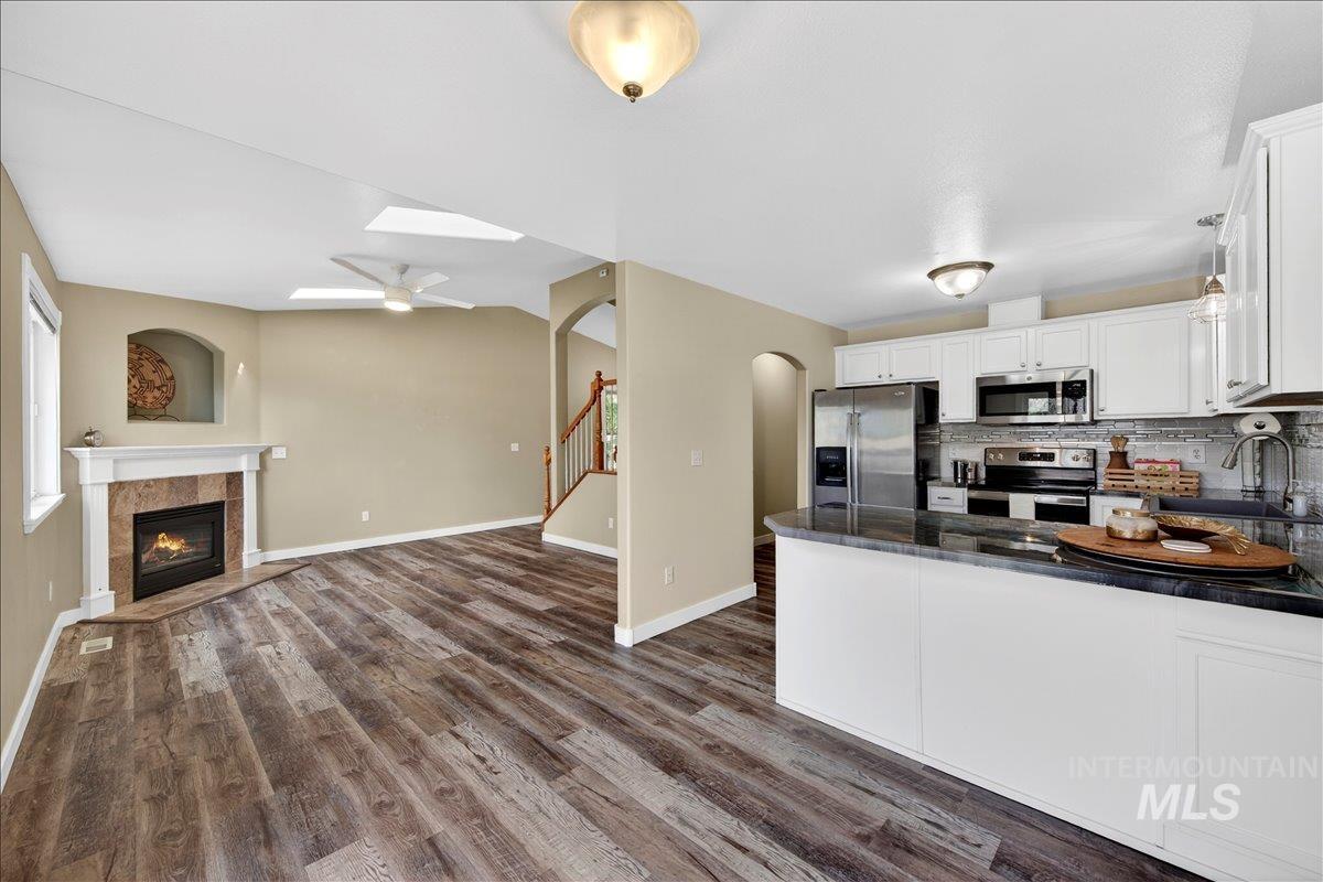Kitchen featuring a tiled fireplace, stainless steel appliances, white cabinetry, open floor plan, and dark wood-type flooring