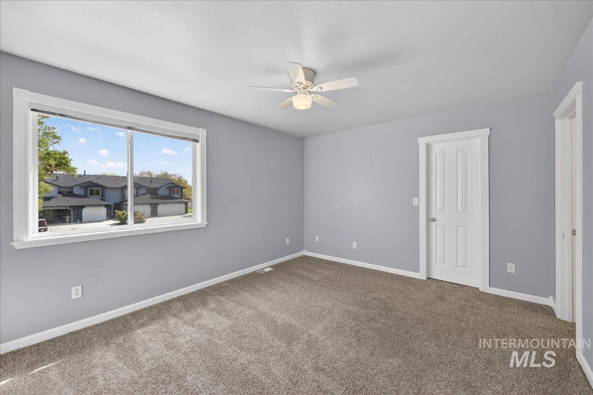 Carpeted spare room with a ceiling fan and baseboards