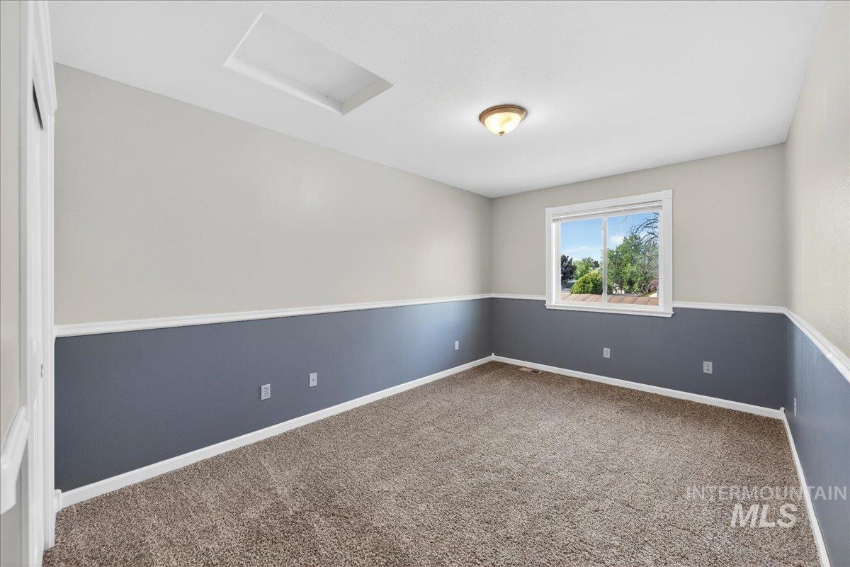 Empty room featuring attic access and dark colored carpet