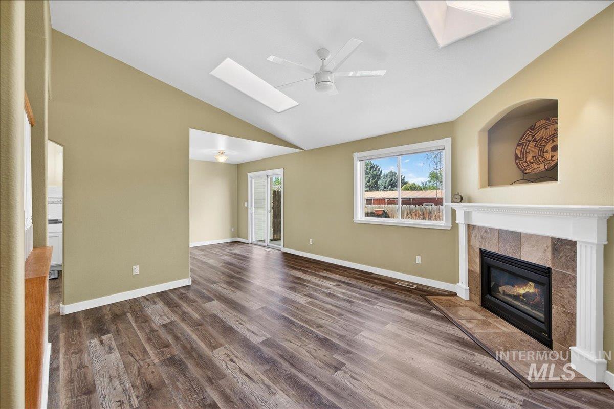 Unfurnished living room featuring a ceiling fan, a skylight, dark wood-style floors, a tile fireplace, and lofted ceiling