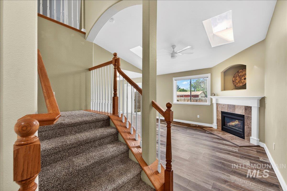 Stairway with a skylight, wood finished floors, a tile fireplace, and ceiling fan