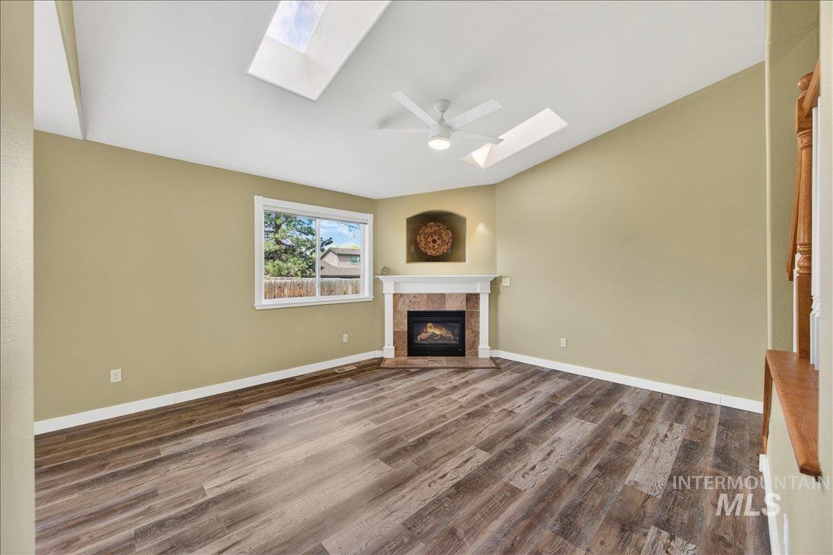 Unfurnished living room featuring a skylight, dark wood-style floors, a tiled fireplace, and a ceiling fan