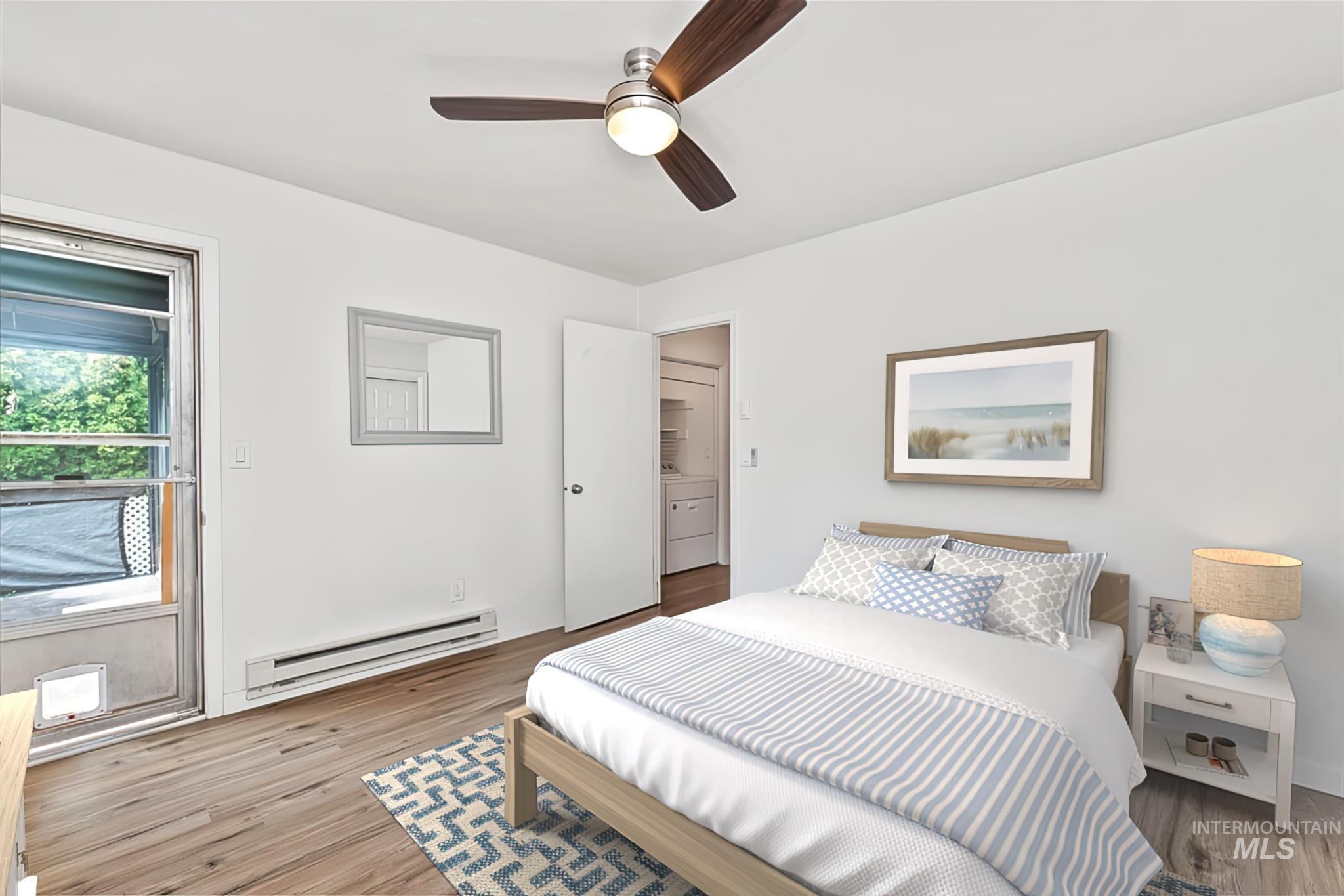 Bedroom with a baseboard heating unit, wood finished floors, ceiling fan, and washer / clothes dryer