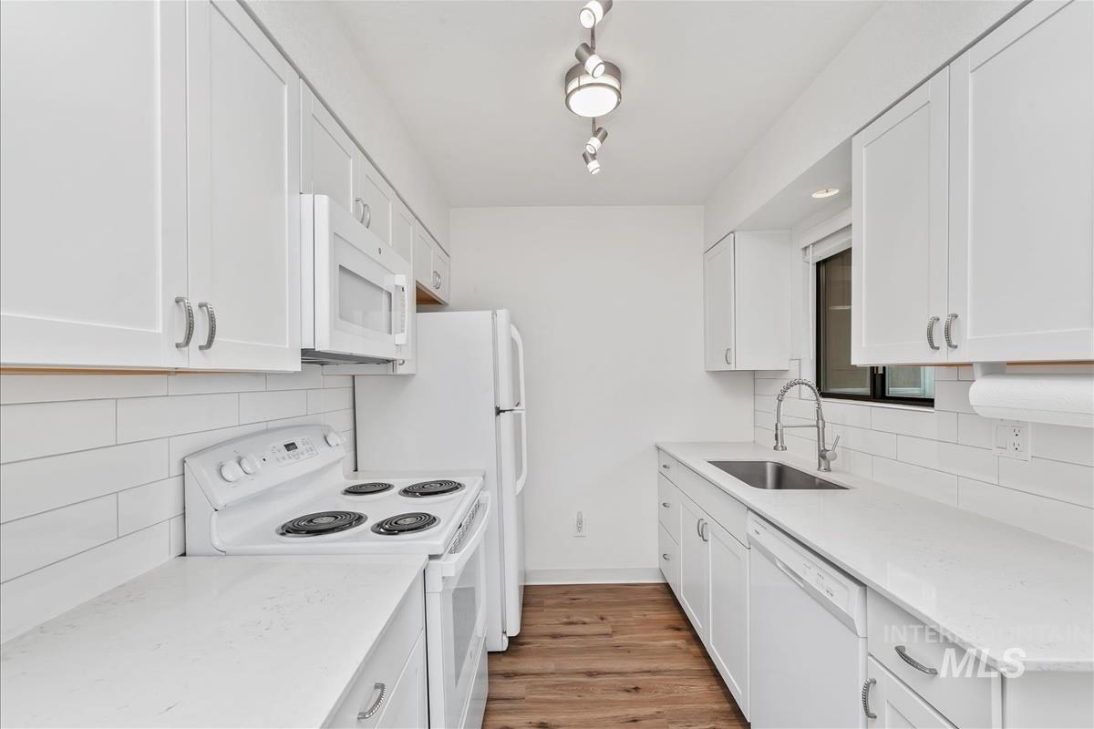 Kitchen with white appliances, white cabinets, light stone countertops, and light wood-style flooring
