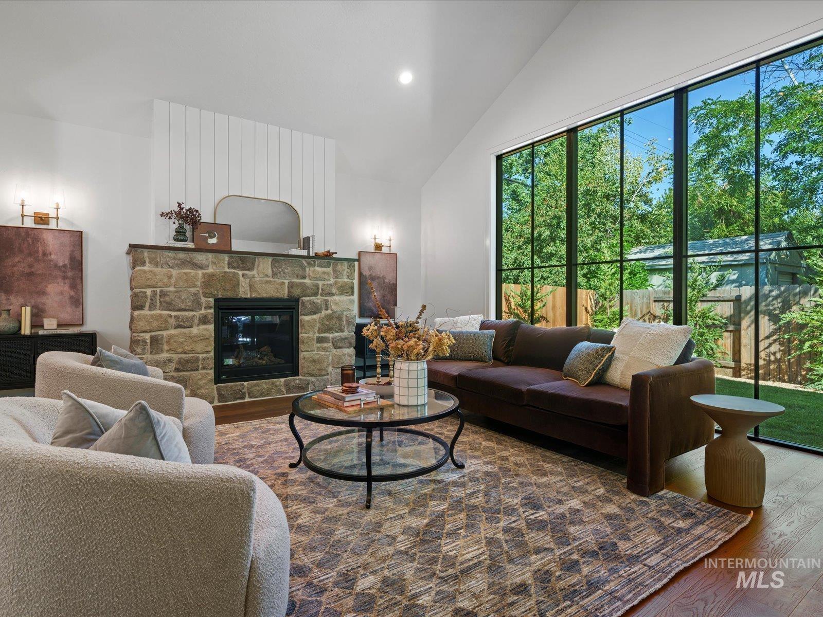 Living area featuring wood finished floors, a stone fireplace, recessed lighting, and high vaulted ceiling