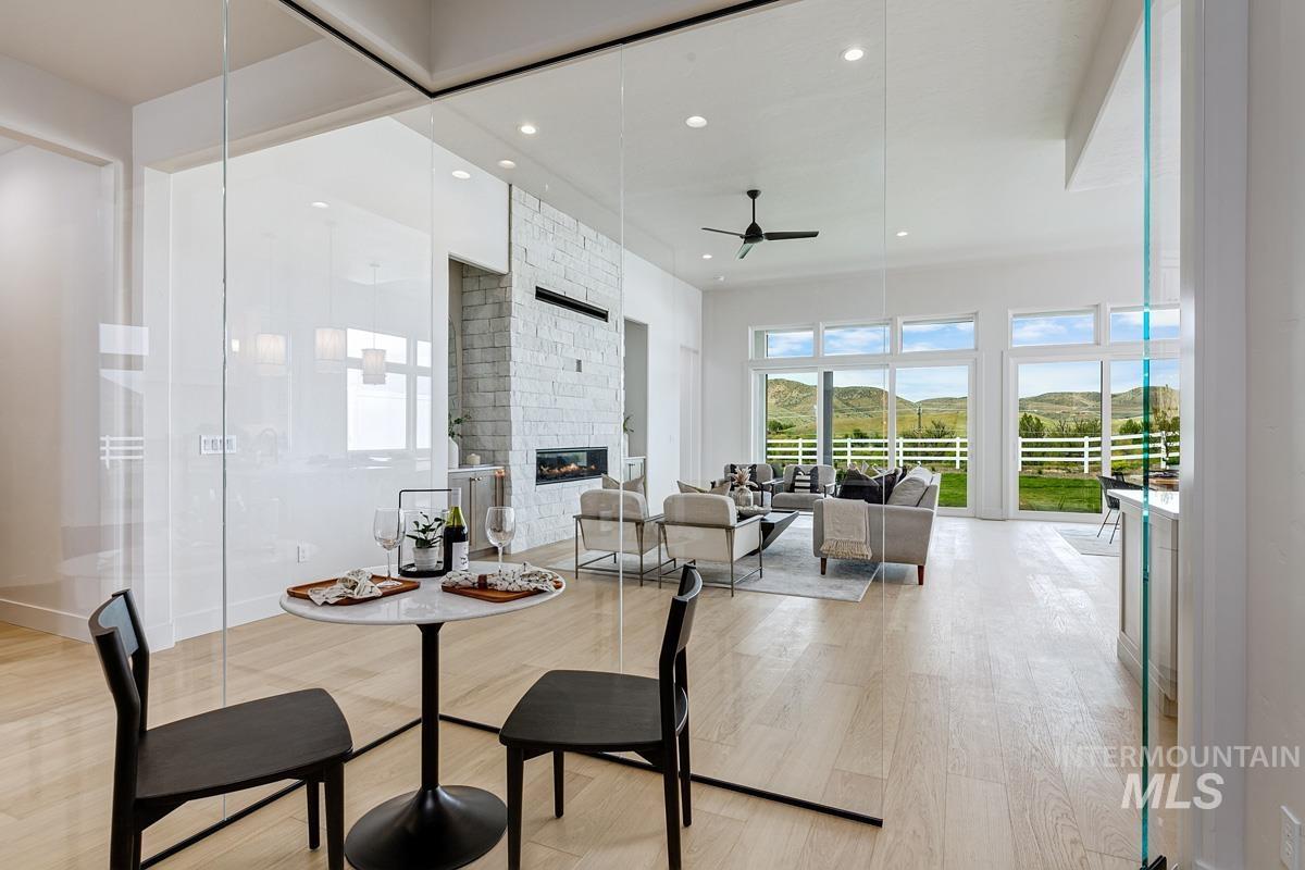 Dining room featuring a ceiling fan, light wood finished floors, a stone fireplace, recessed lighting, and a high ceiling