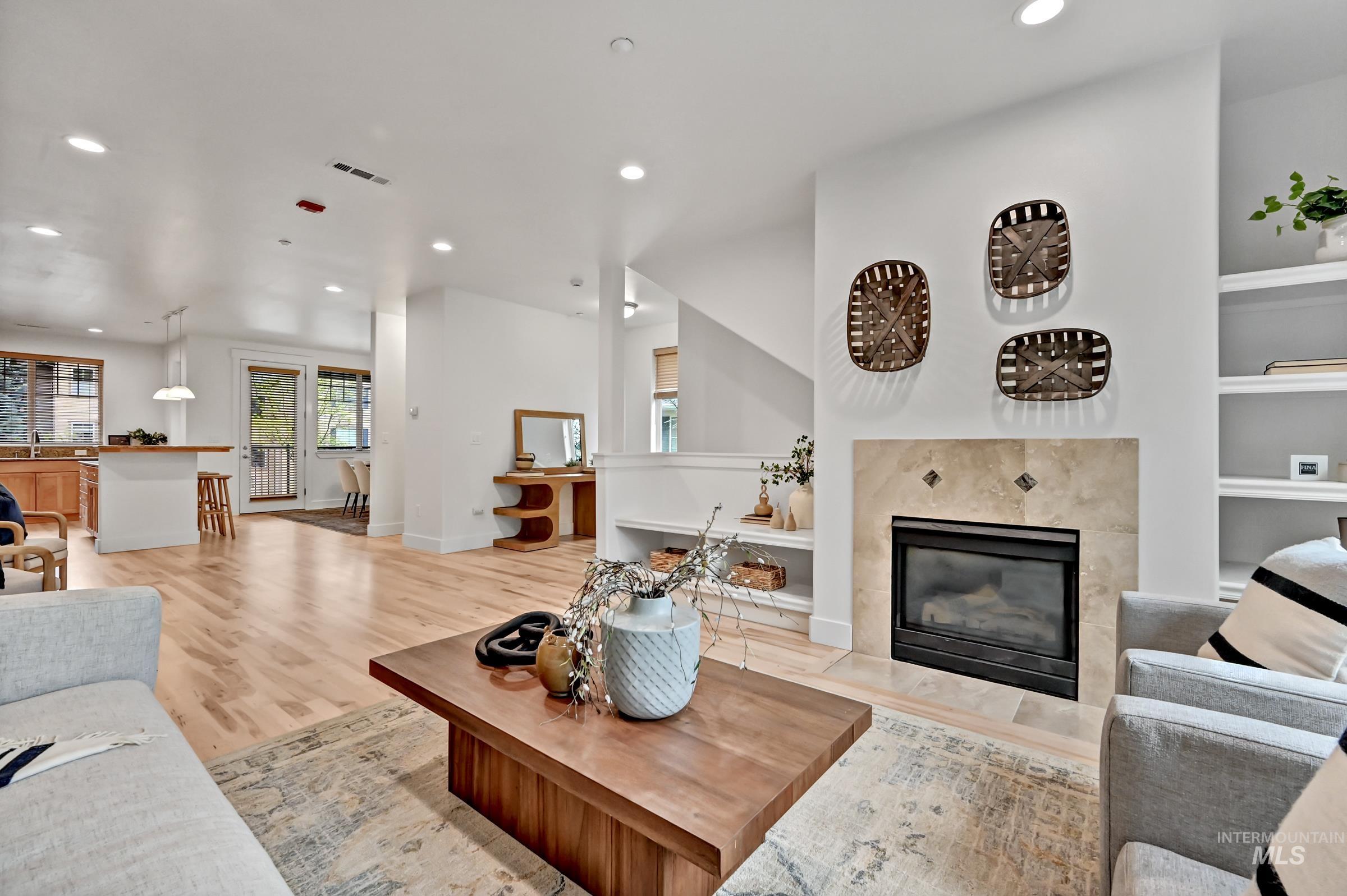 Open living and dining area with hardwood floors and a fireplace. Bright layout with natural light and functional flow.