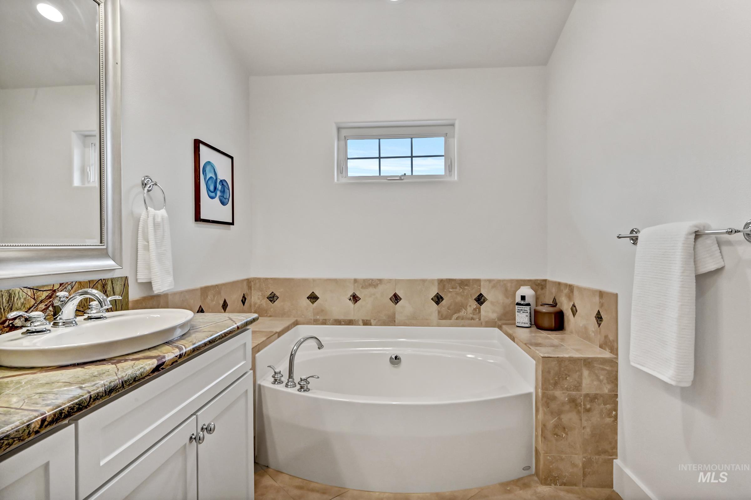 Bathroom with tile floors, a soaking tub, and a window above the tub. Clean, spacious layout suited for relaxation.