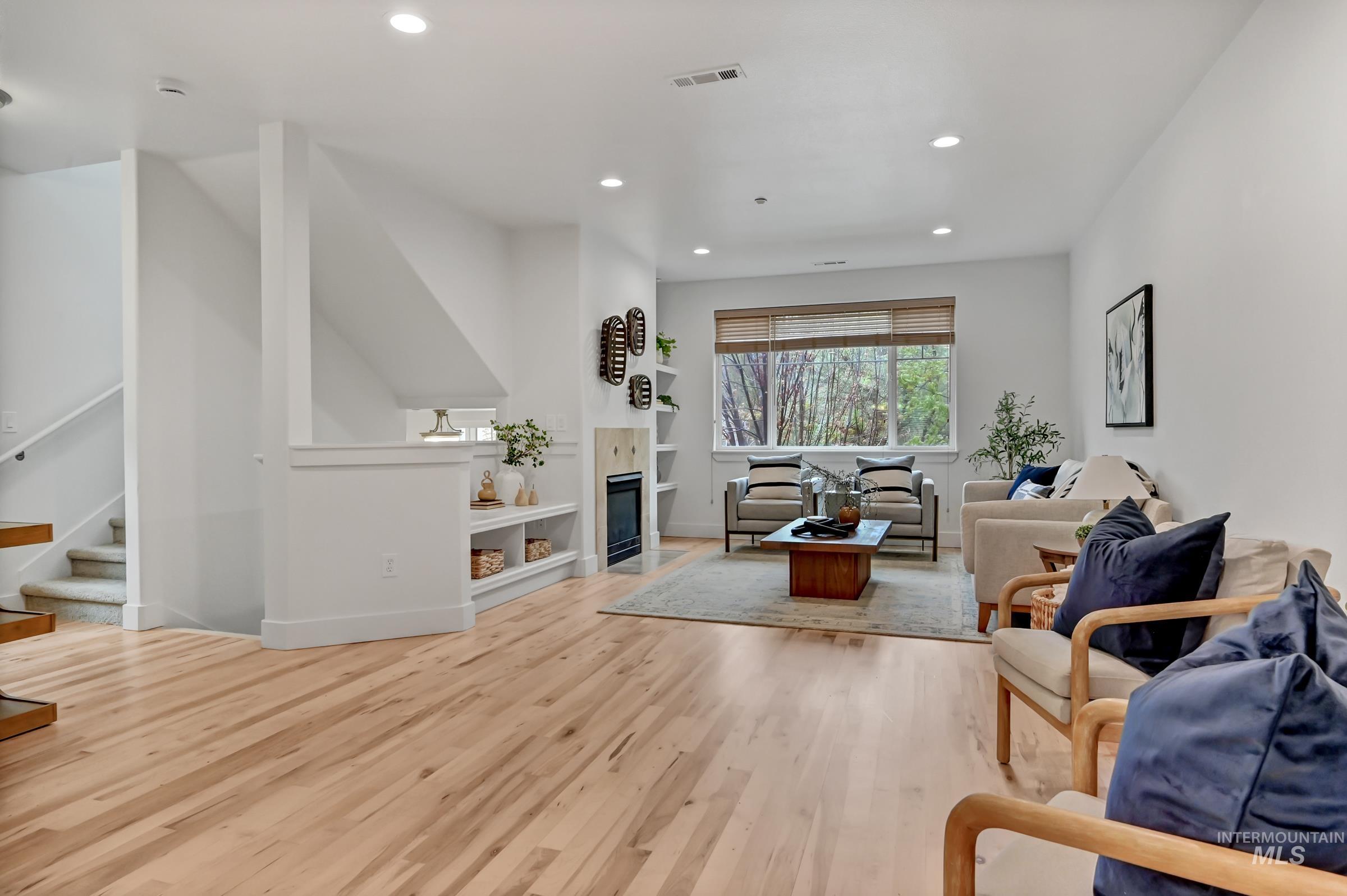 Spacious living room with hardwood floors and a fireplace. Bright space with clean finishes and natural light from large windows.