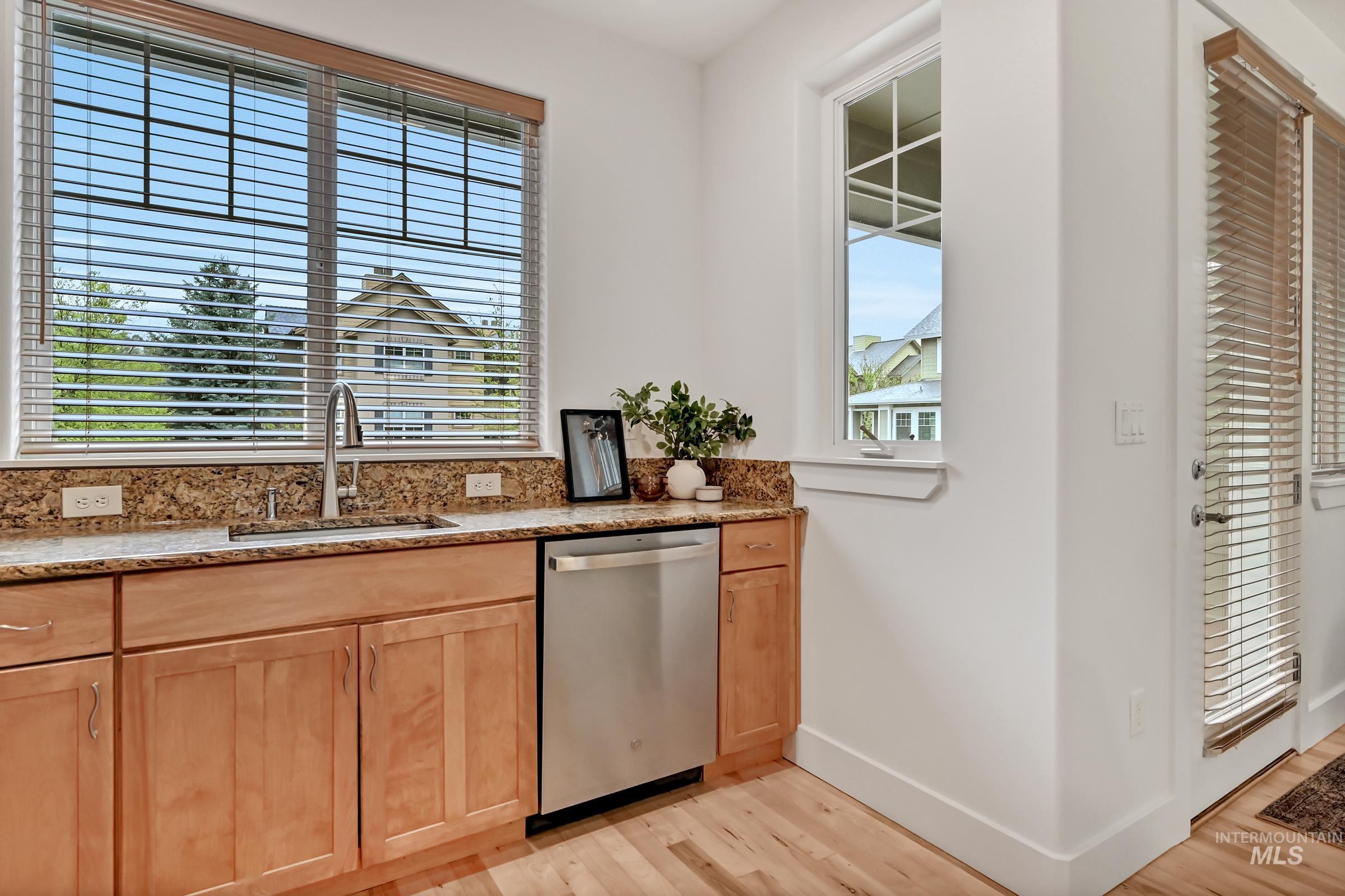 Kitchen sink area with granite counters, dishwasher, and window above. Bright workspace with clean cabinetry.