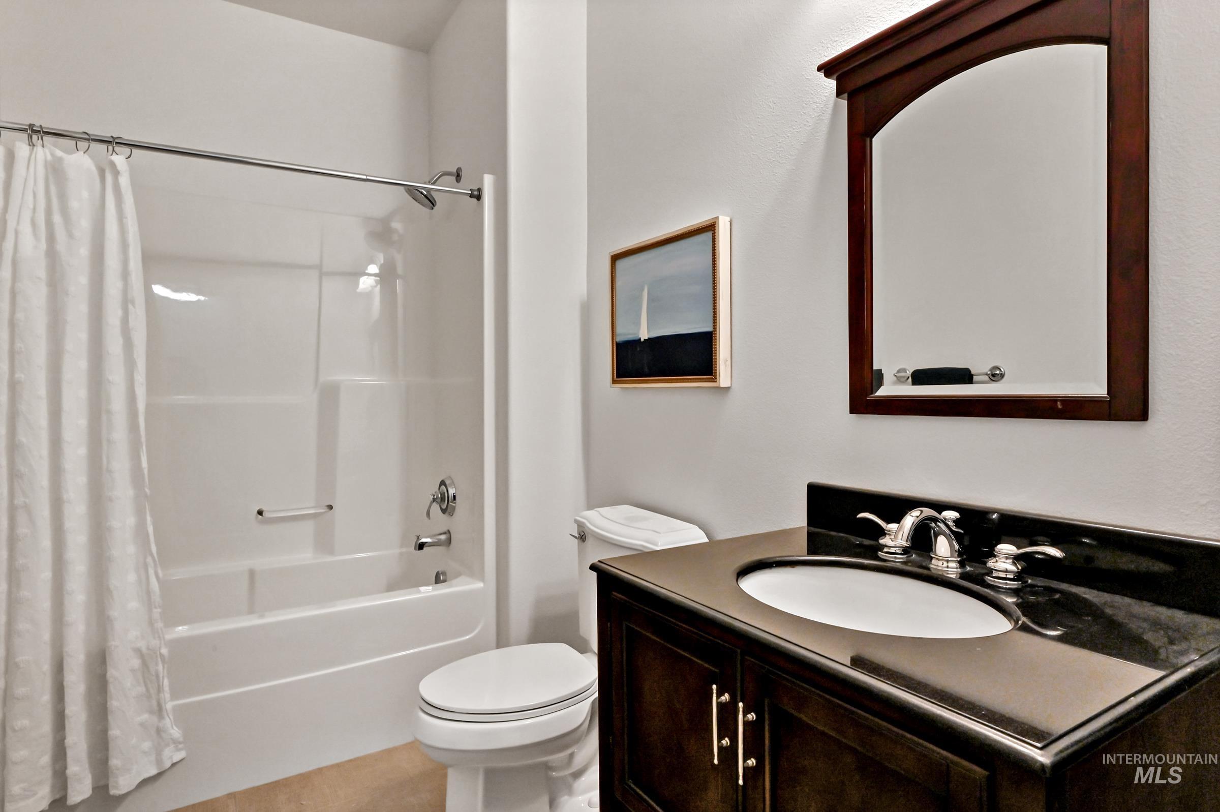 First-level bathroom with wood vanity, framed mirror, and tile flooring. Tub/shower insert. Functional design with clean finishes.