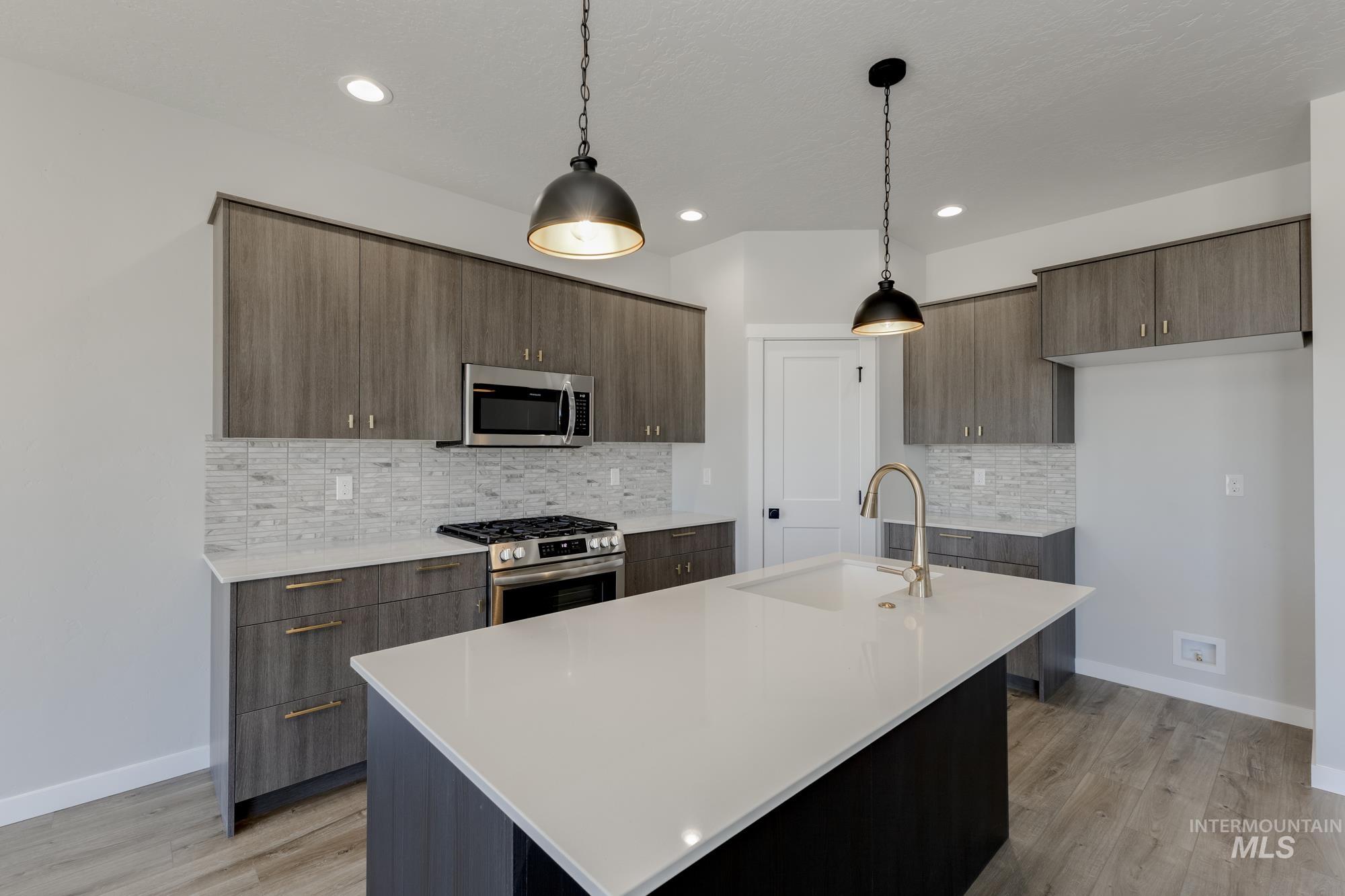 Kitchen with modern cabinets, stainless steel appliances, decorative light fixtures, a center island with sink, and recessed lighting