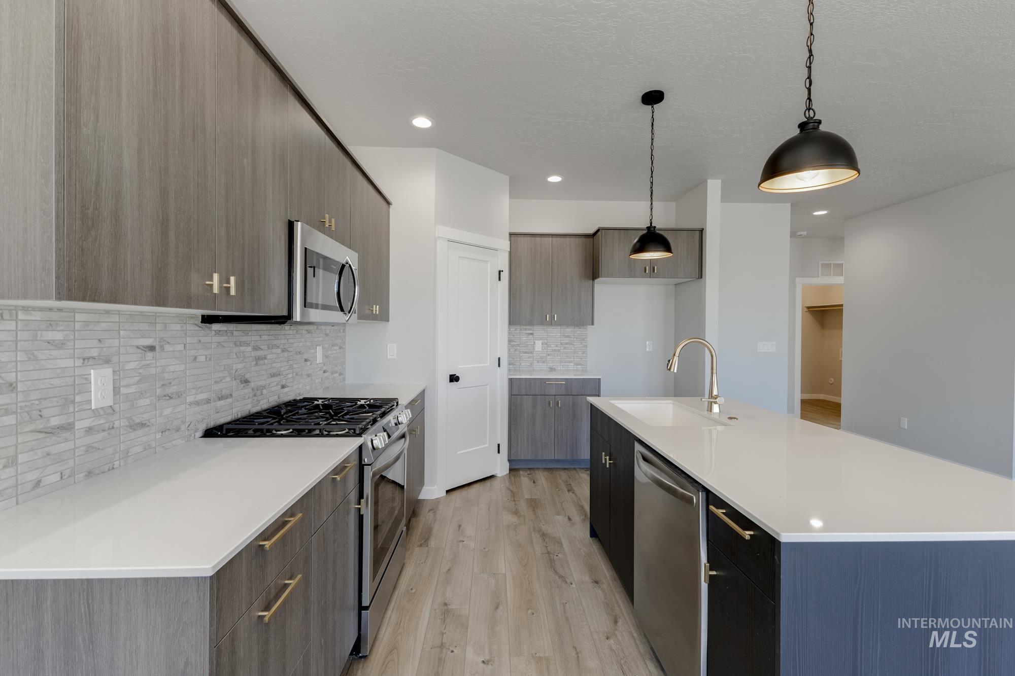 Kitchen featuring stainless steel appliances, decorative light fixtures, light wood-type flooring, an island with sink, and modern cabinets
