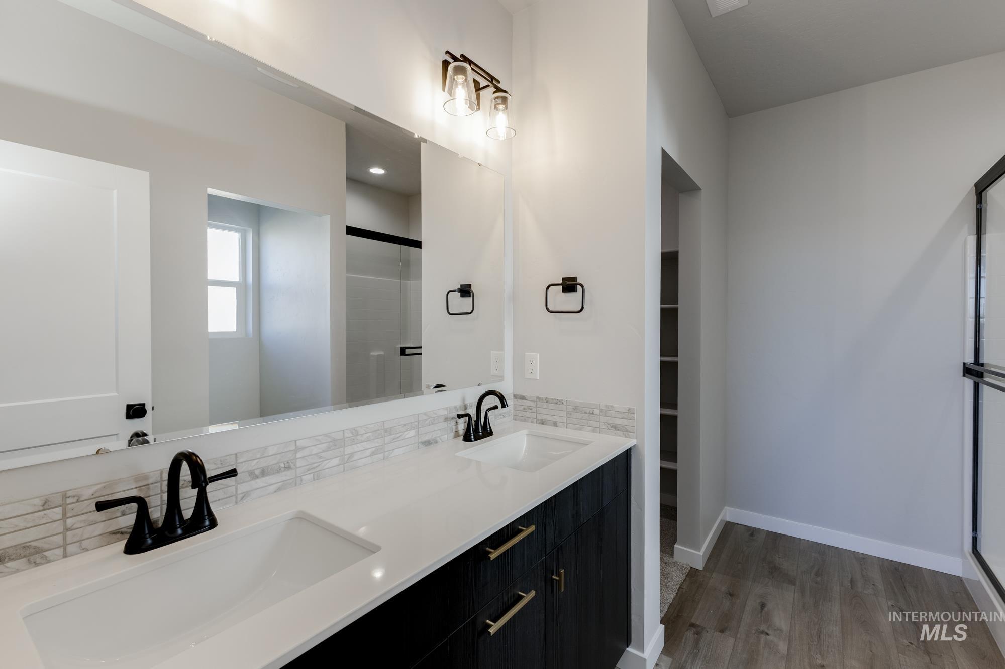 Full bath with a shower stall, double vanity, light wood-type flooring, decorative backsplash, and a walk in closet