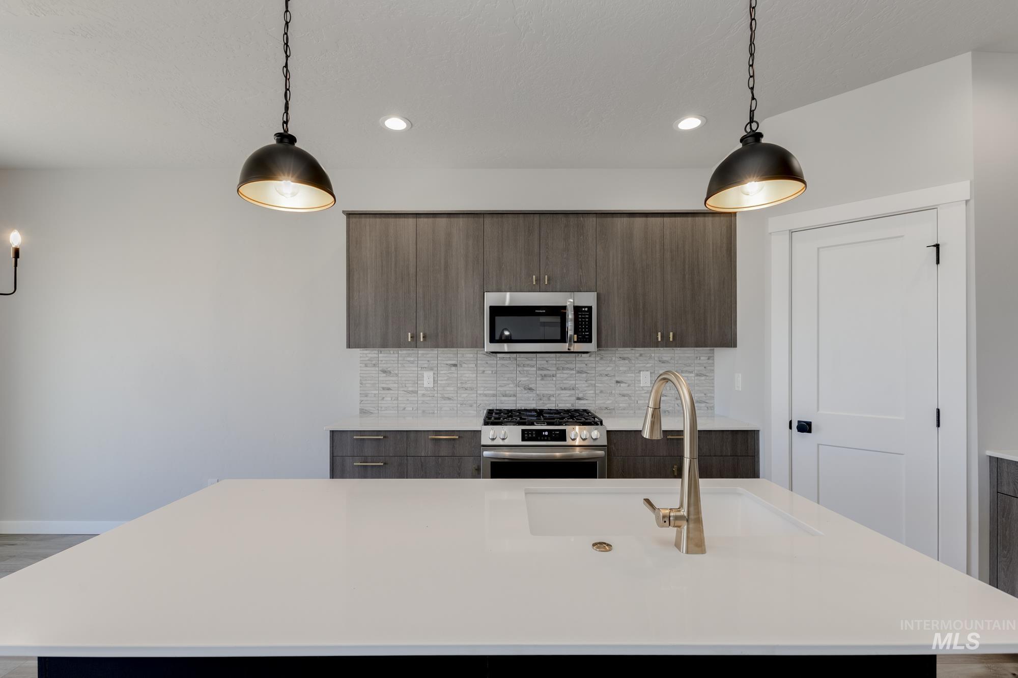 Kitchen featuring a center island with sink, appliances with stainless steel finishes, modern cabinets, tasteful backsplash, and light stone counters
