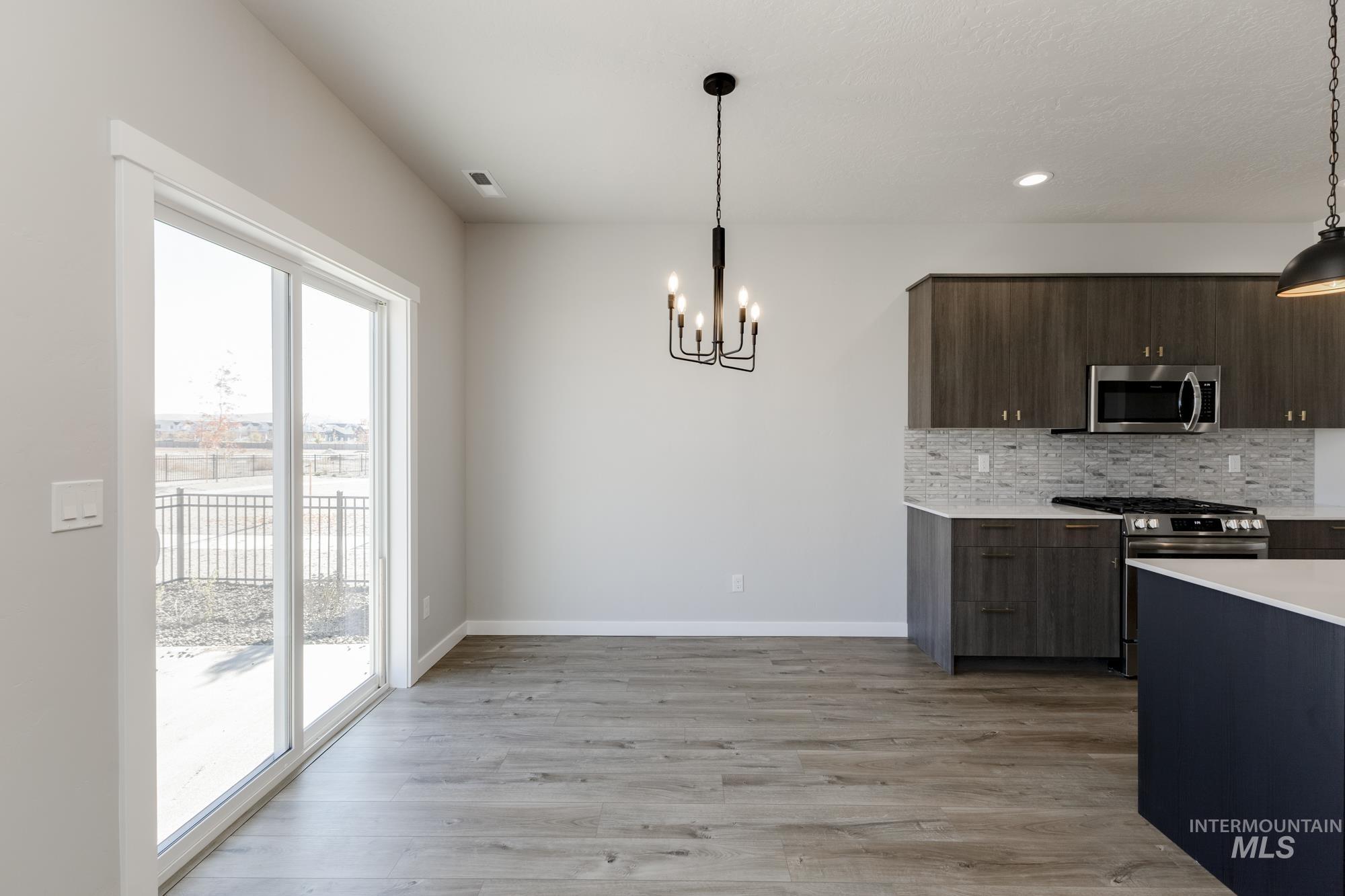Kitchen featuring appliances with stainless steel finishes, backsplash, a chandelier, light wood-style flooring, and modern cabinets