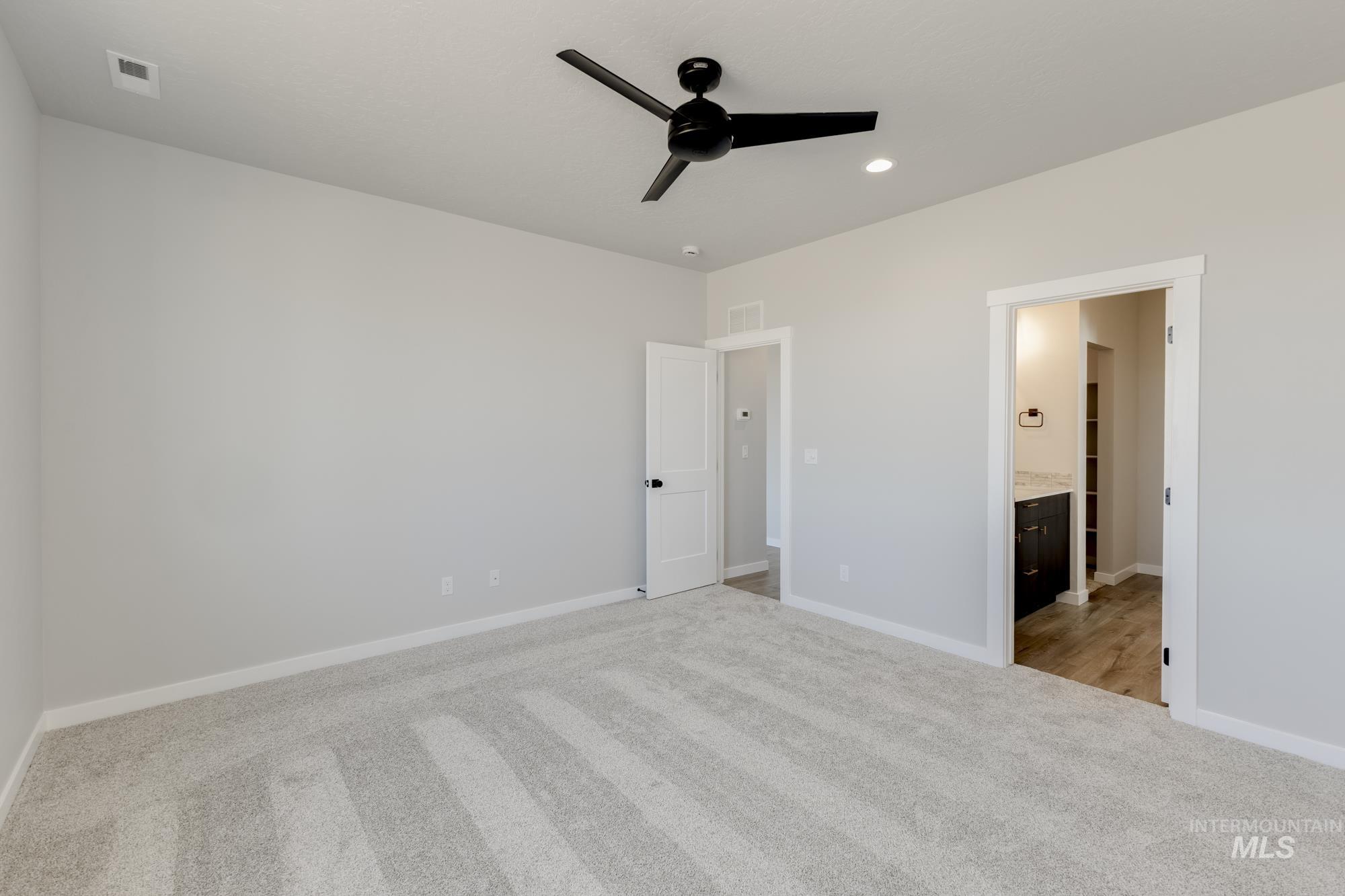 Unfurnished bedroom featuring light colored carpet, ceiling fan, and ensuite bathroom