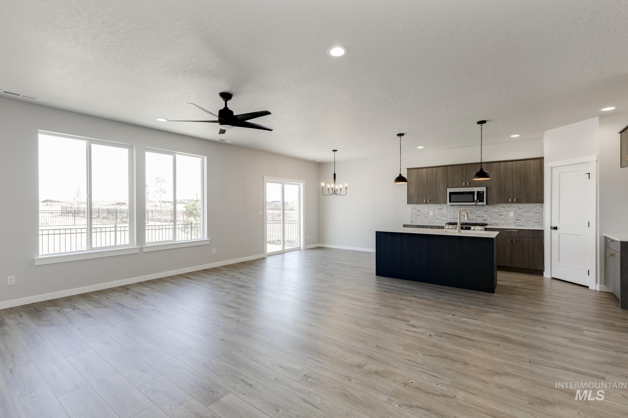 Kitchen featuring open floor plan, pendant lighting, an island with sink, recessed lighting, and stainless steel microwave