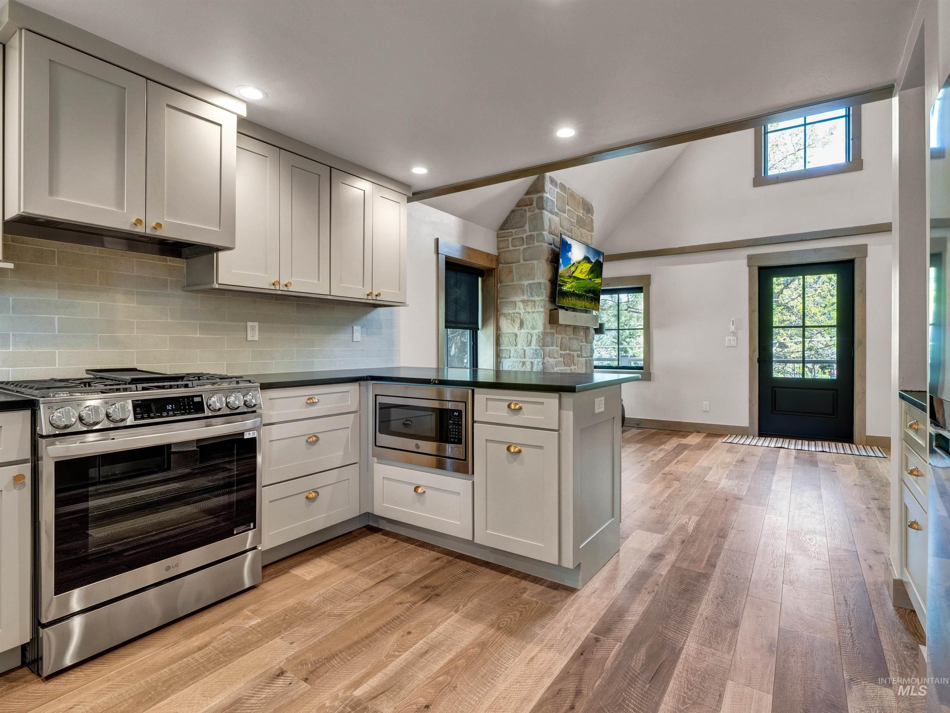 Kitchen with stainless steel appliances, a peninsula, light wood-style floors, vaulted ceiling, and backsplash