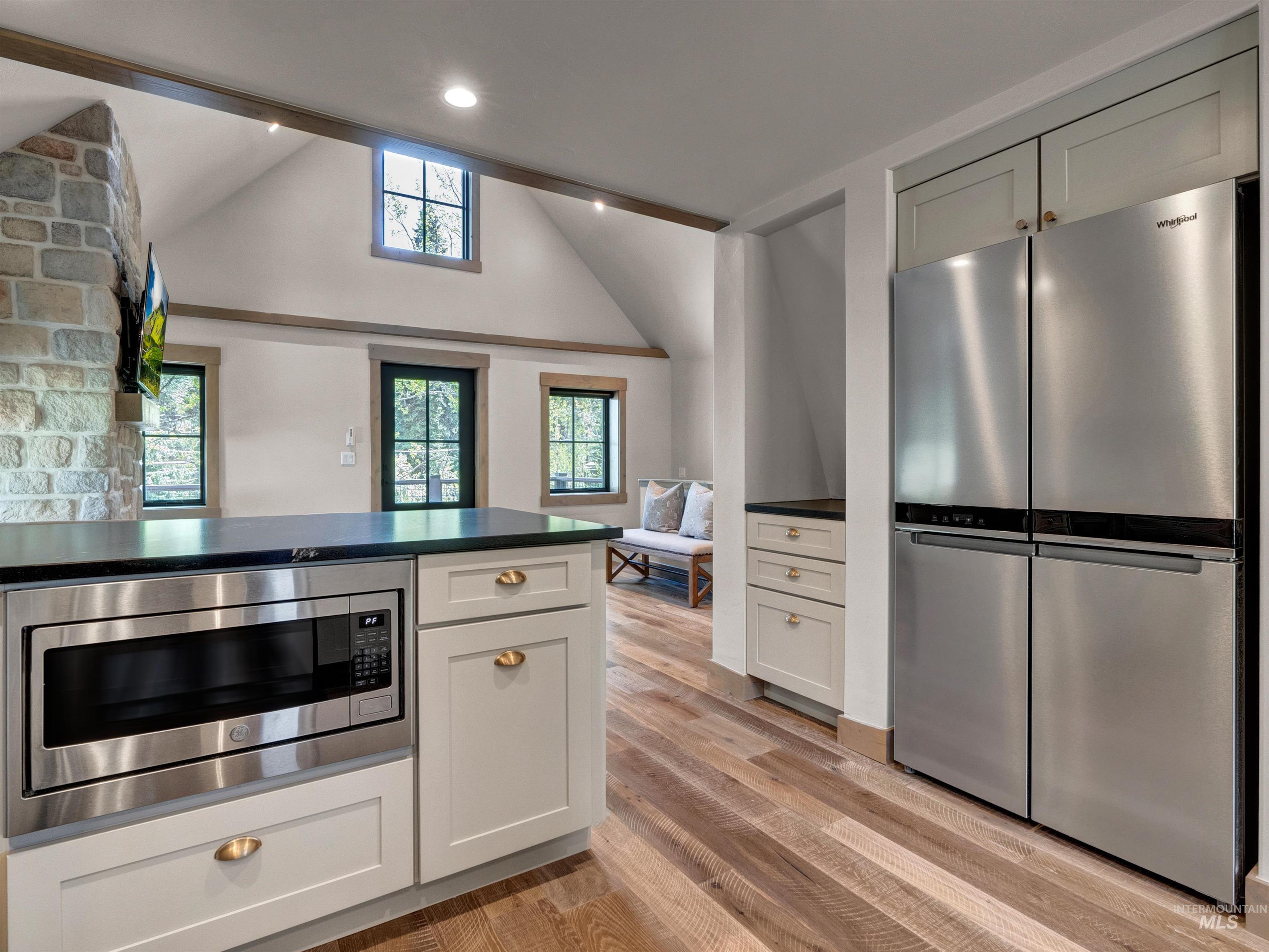 Kitchen featuring stainless steel appliances, dark countertops, light wood-type flooring, and vaulted ceiling