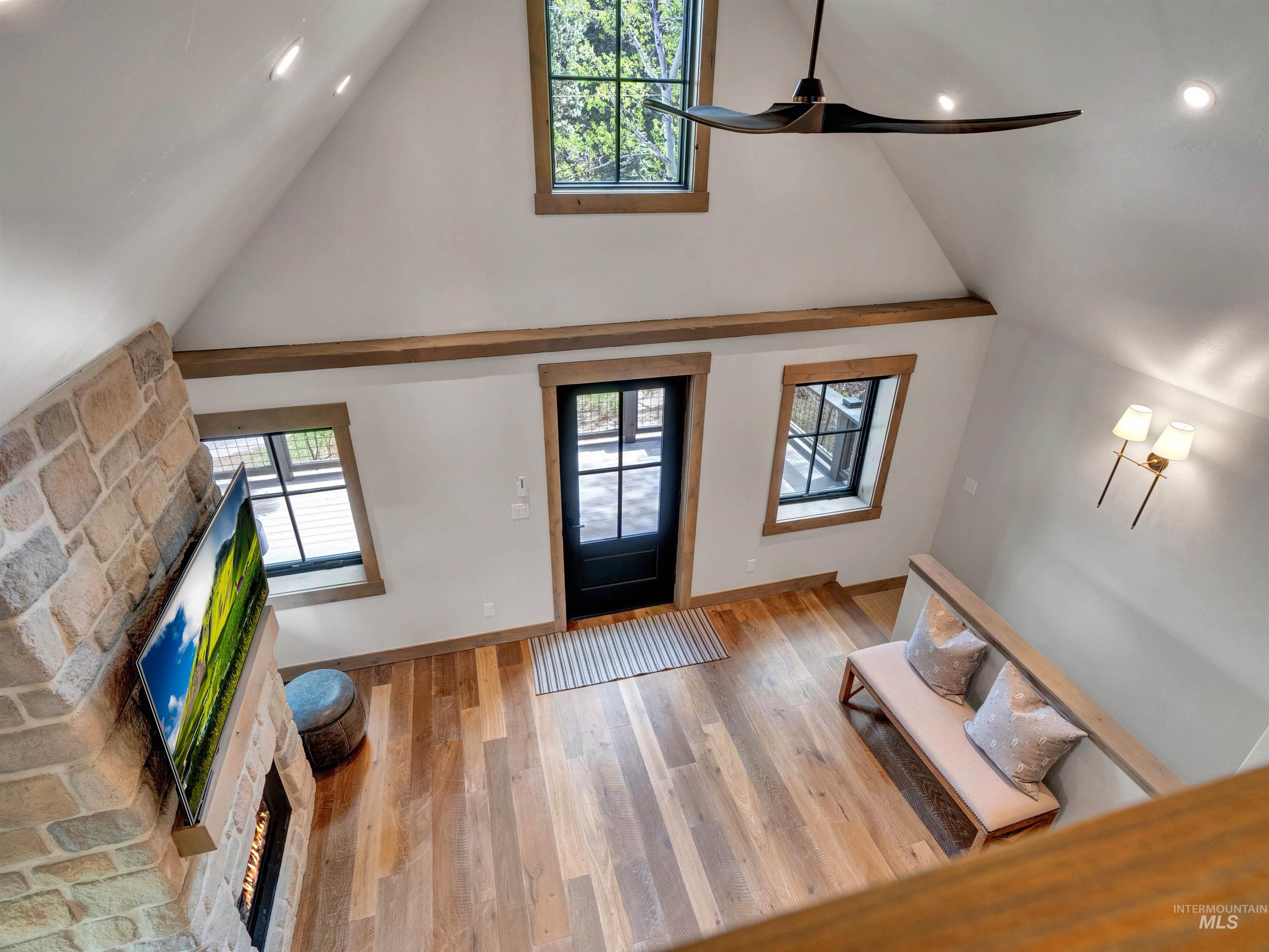 Entryway featuring a stone fireplace, wood finished floors, a ceiling fan, and a high ceiling