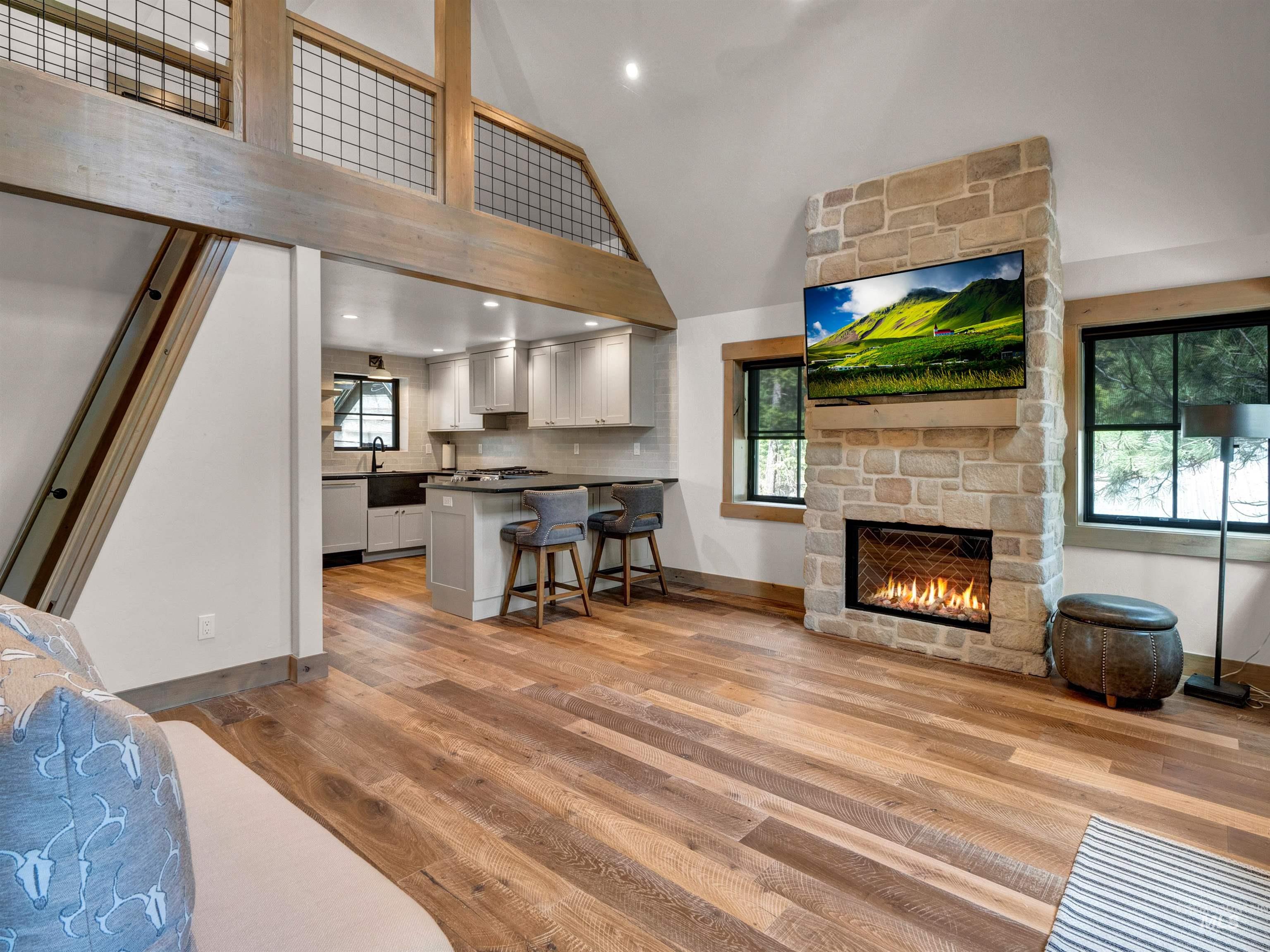 Living area with a stone fireplace, light wood finished floors, lofted ceiling, and recessed lighting