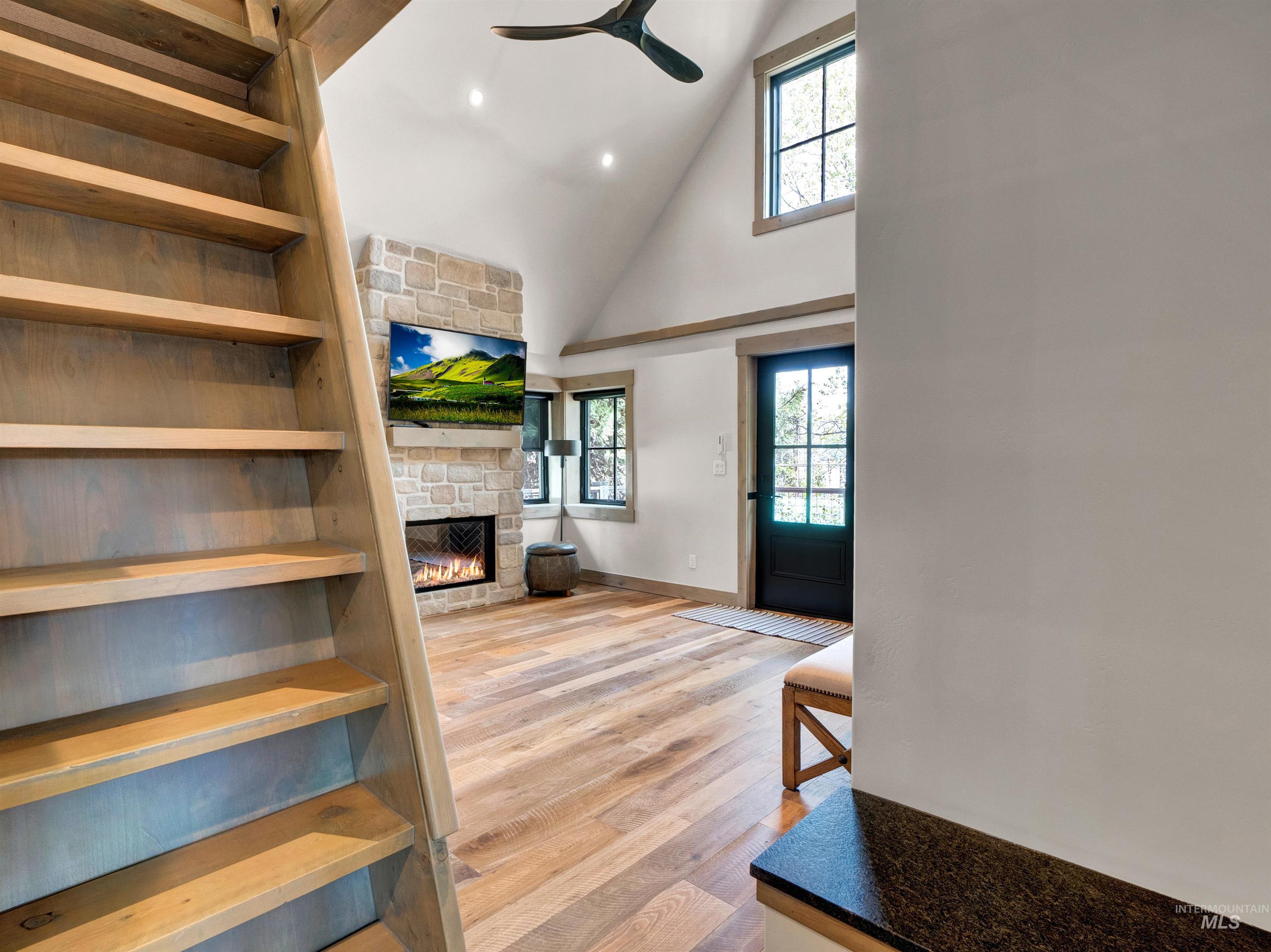 Living area with light wood-style flooring, a ceiling fan, lofted ceiling, recessed lighting, and a stone fireplace