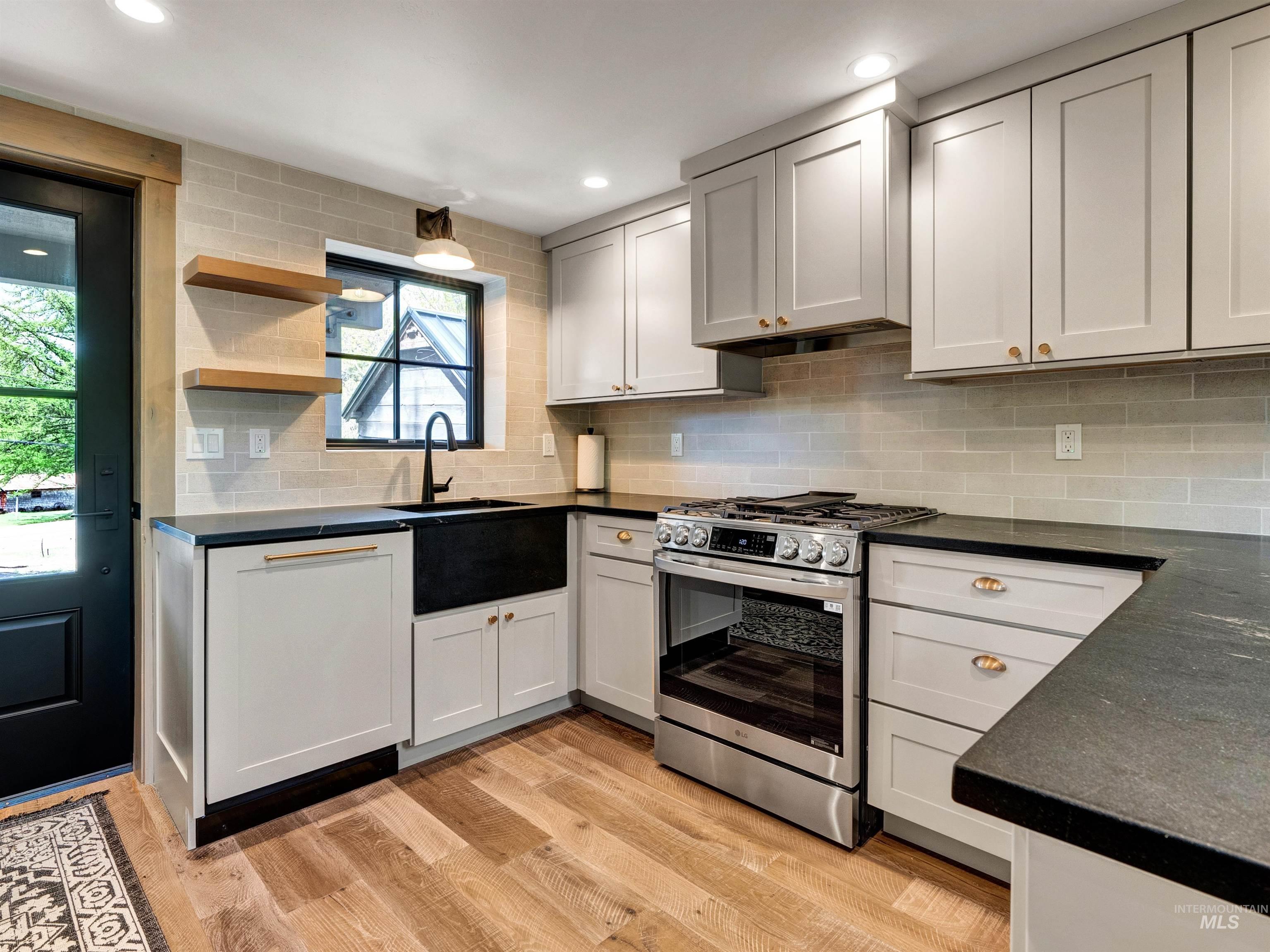 Kitchen with stainless steel gas range, open shelves, light wood finished floors, decorative backsplash, and recessed lighting