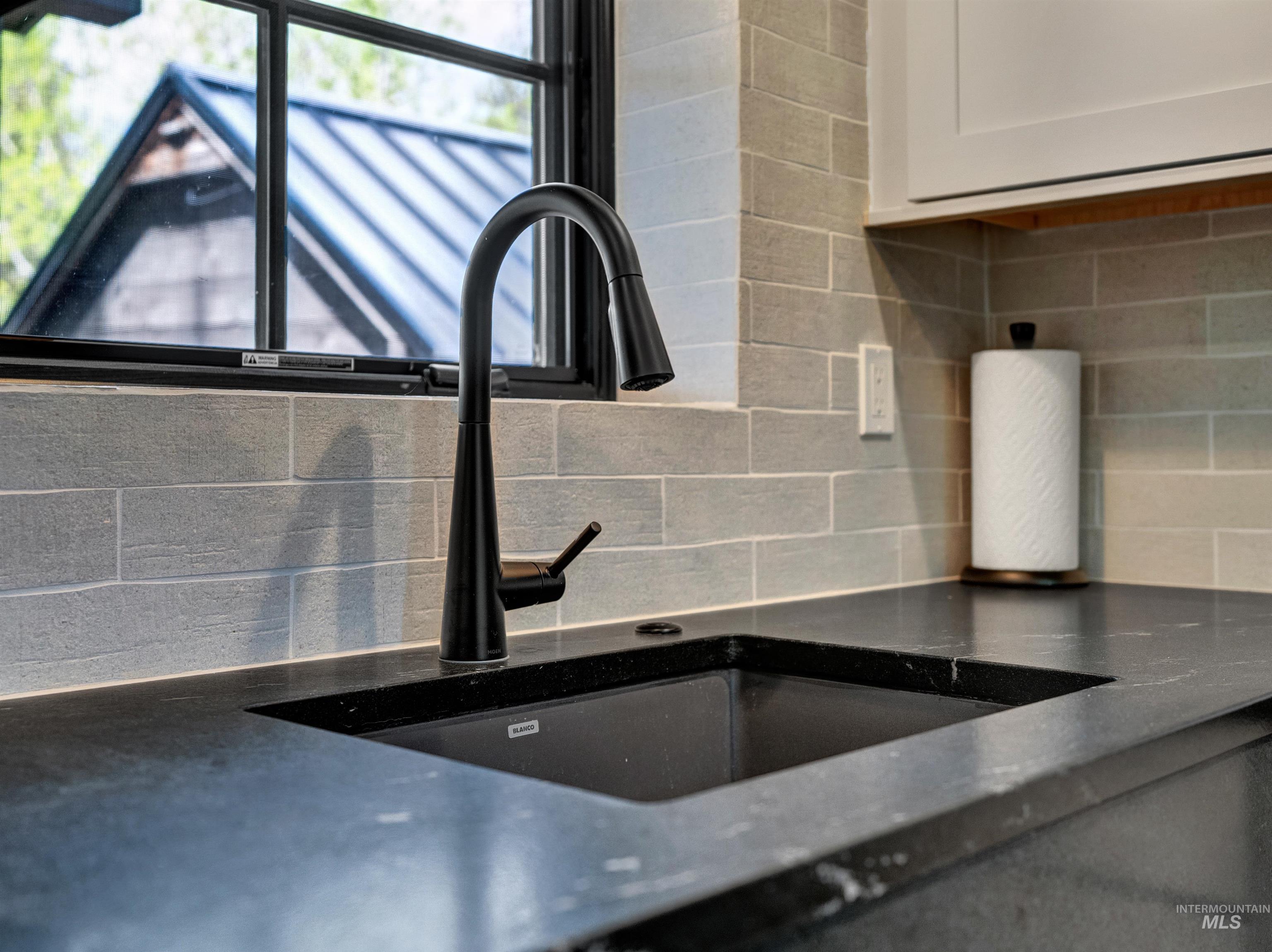 Kitchen view of tasteful backsplash, dark stone counters, and white cabinetry
