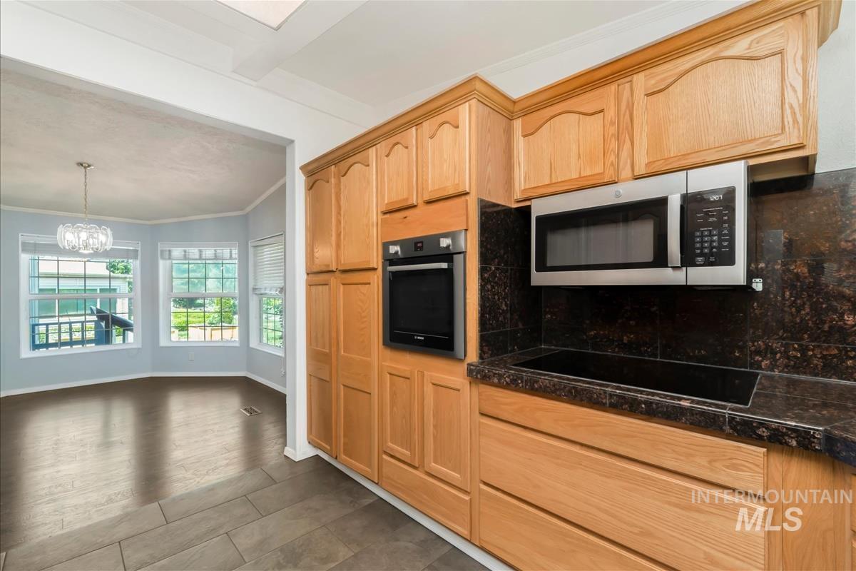 Kitchen featuring black appliances, crown molding, a chandelier, light brown cabinetry, and hanging light fixtures
