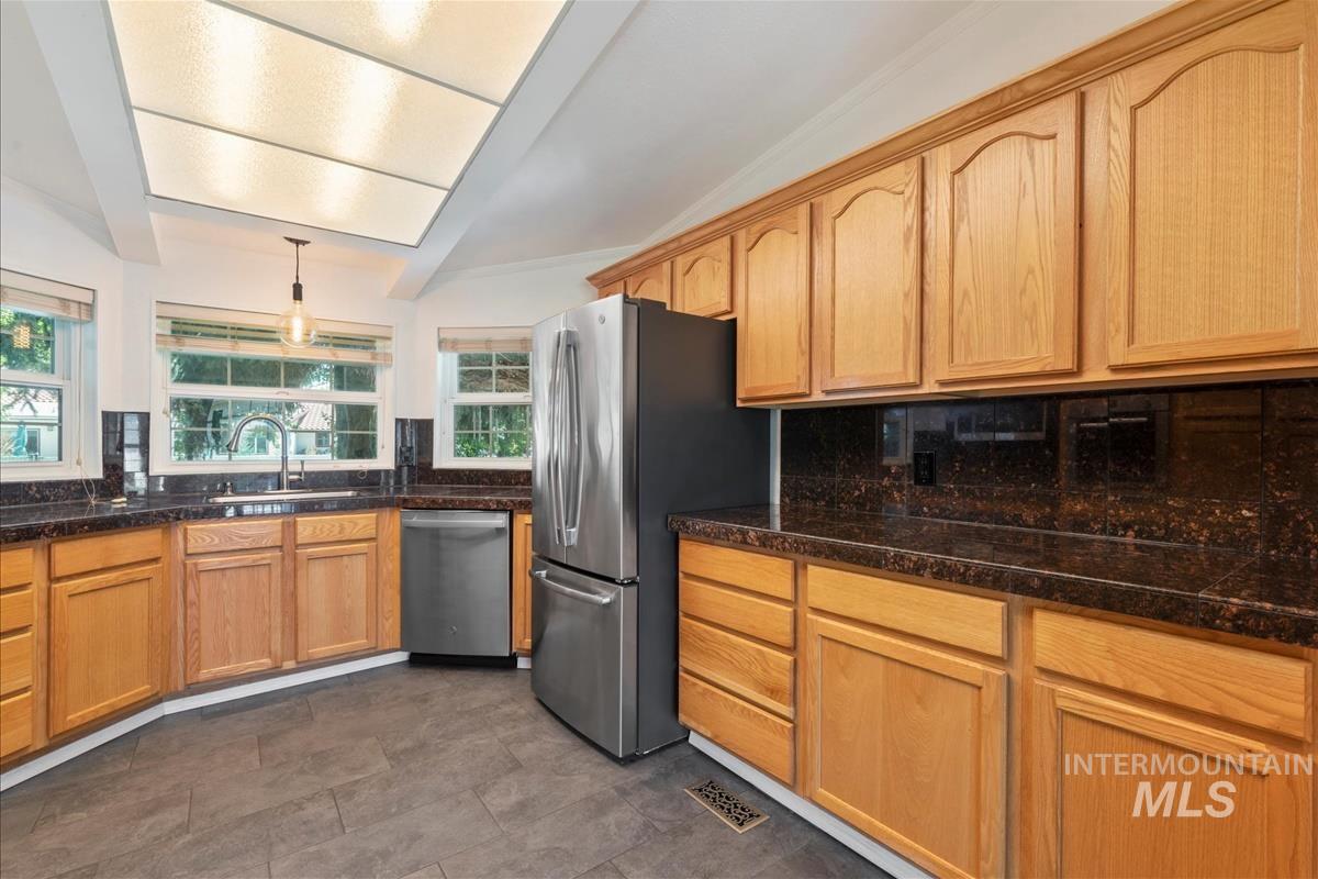 Kitchen featuring appliances with stainless steel finishes, backsplash, pendant lighting, and dark stone countertops