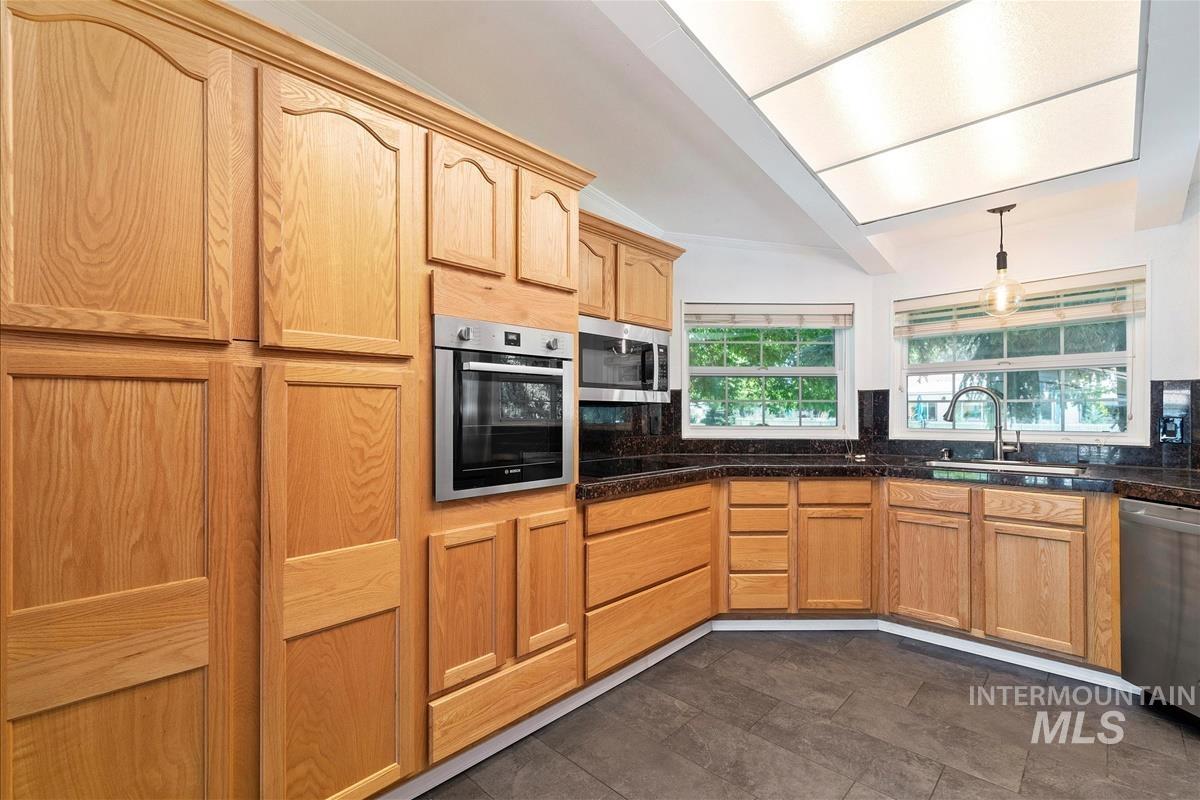 Kitchen with appliances with stainless steel finishes, dark countertops, lofted ceiling, hanging light fixtures, and decorative backsplash