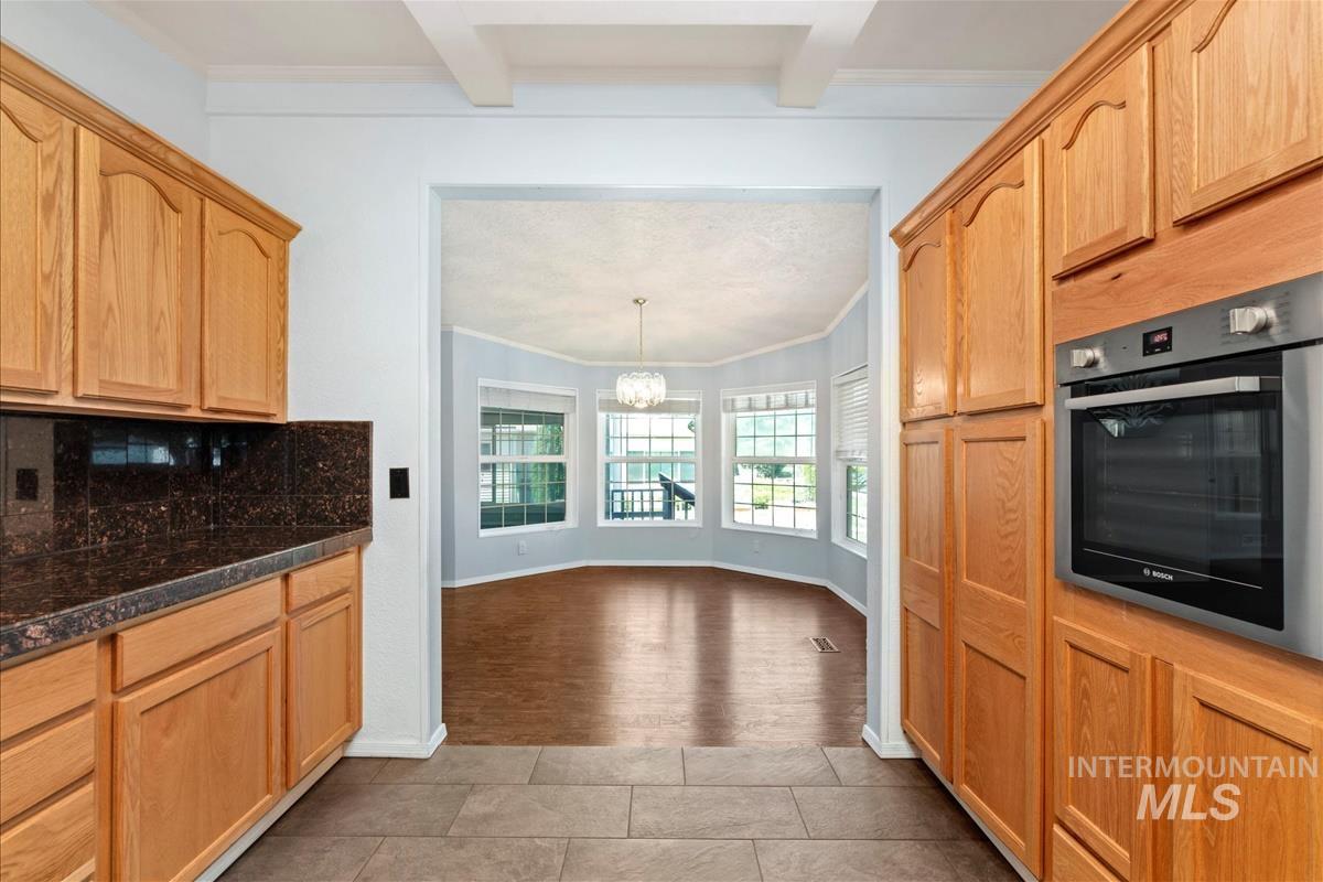 Kitchen with oven, beam ceiling, ornamental molding, a chandelier, and decorative backsplash