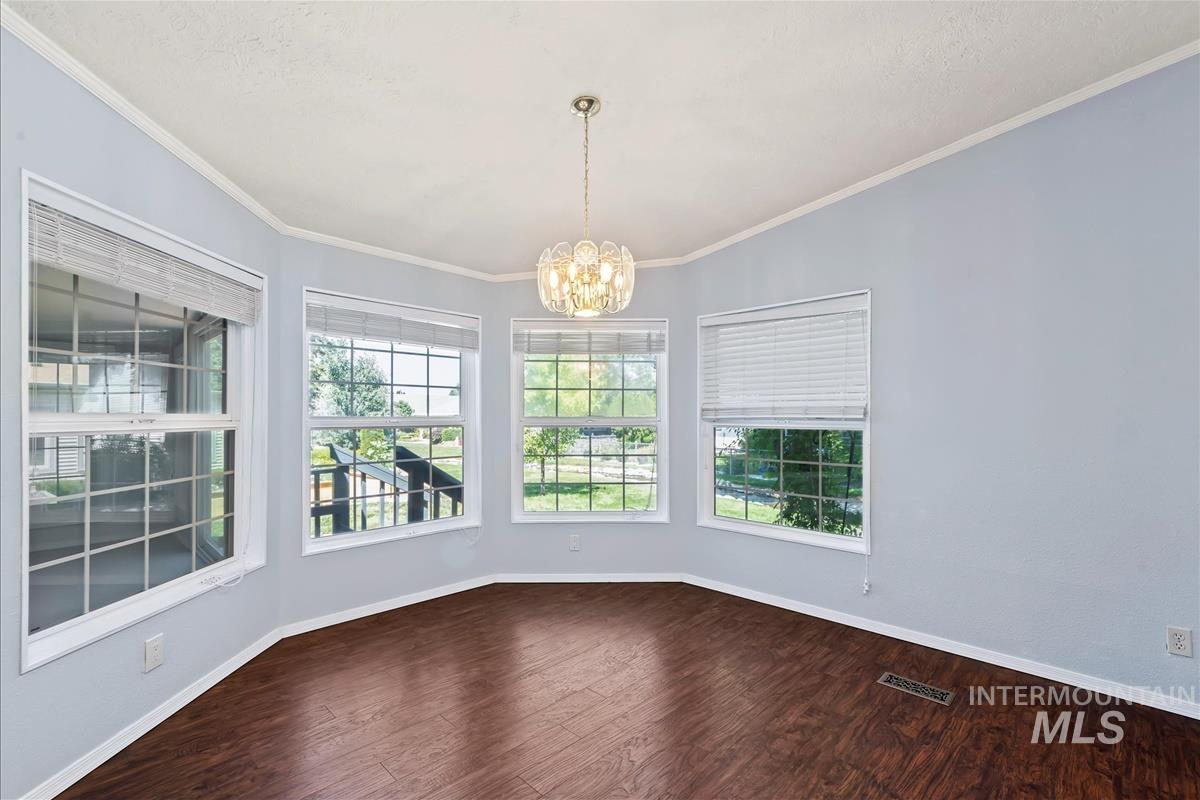 Spare room featuring a chandelier, dark wood-style flooring, and crown molding