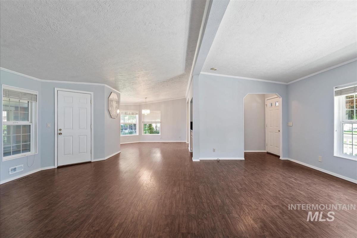 Unfurnished living room with a textured ceiling, dark wood finished floors, arched walkways, plenty of natural light, and crown molding