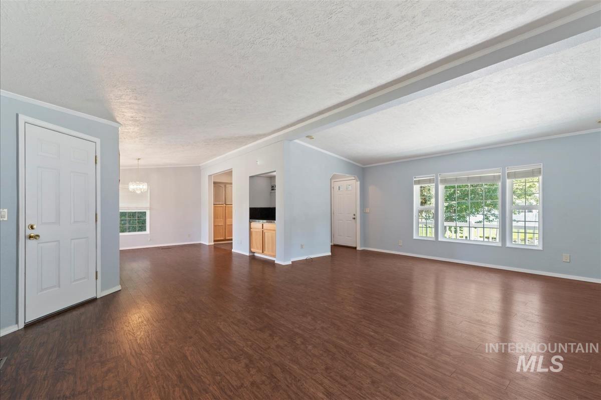 Unfurnished living room featuring a chandelier, a textured ceiling, dark wood-type flooring, ornamental molding, and arched walkways
